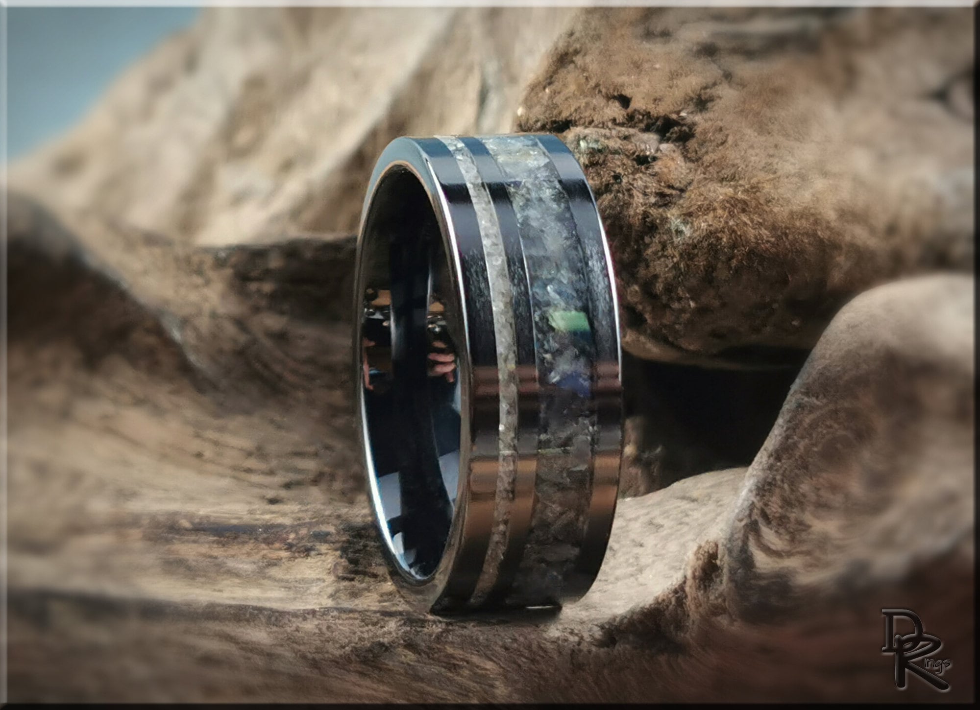Black ceramic ring with dual inlays featuring metallic and stone patterns on wooden background