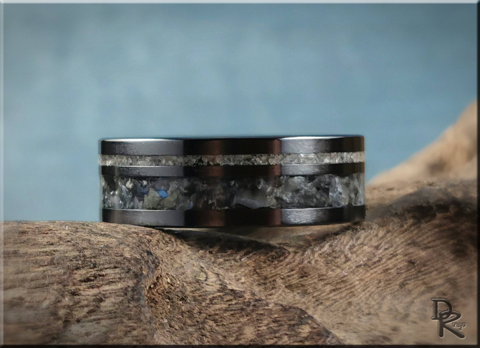 Black ceramic ring with dual inlays featuring stone design on rustic wooden surface by DR Rings