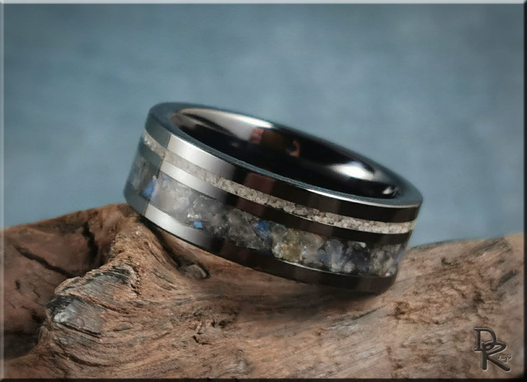 Black ceramic ring with dual inlays featuring metallic and stone accents on wood background