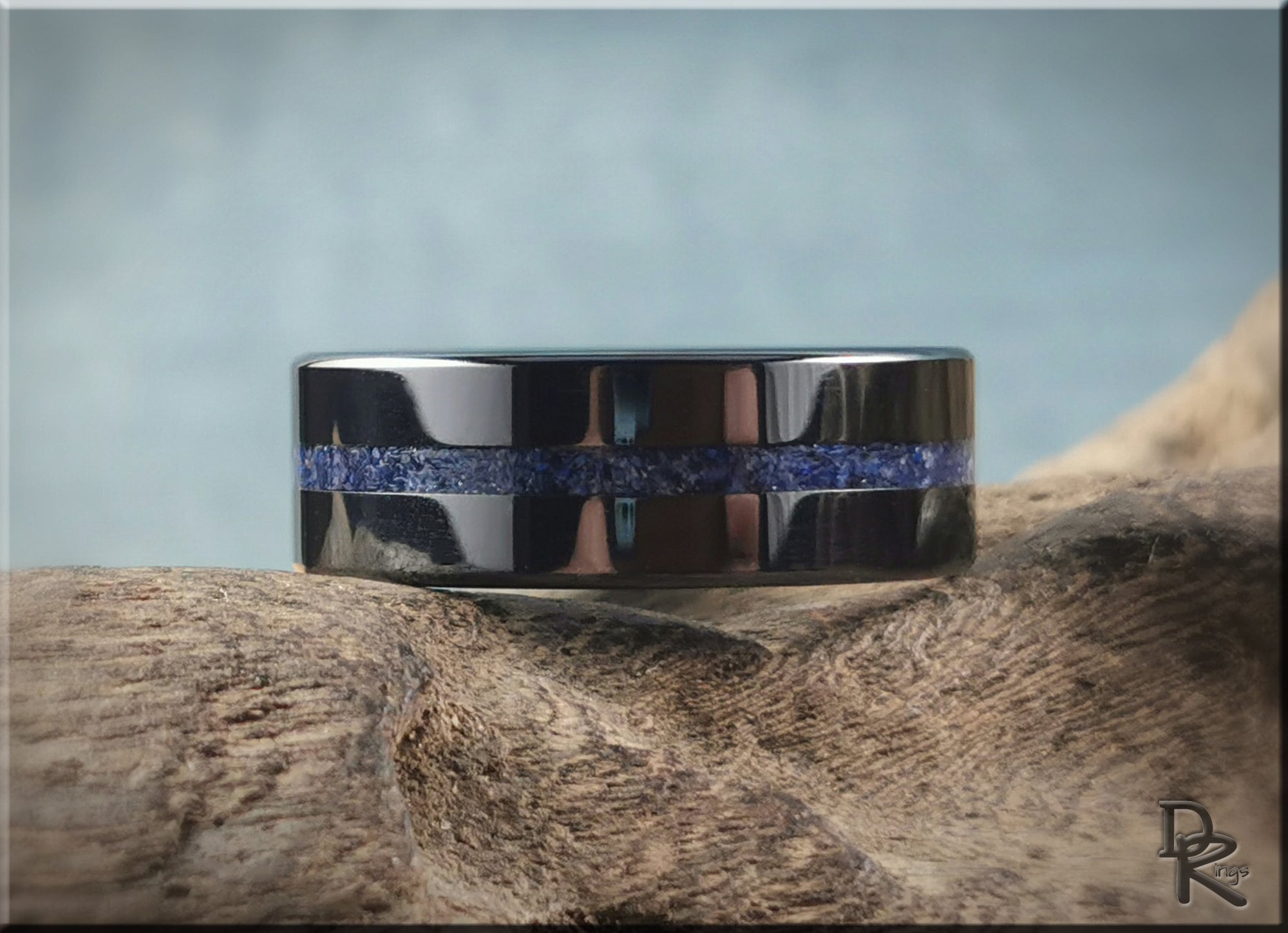 Black ceramic ring with a textured blue inlay band displayed on a natural wooden surface