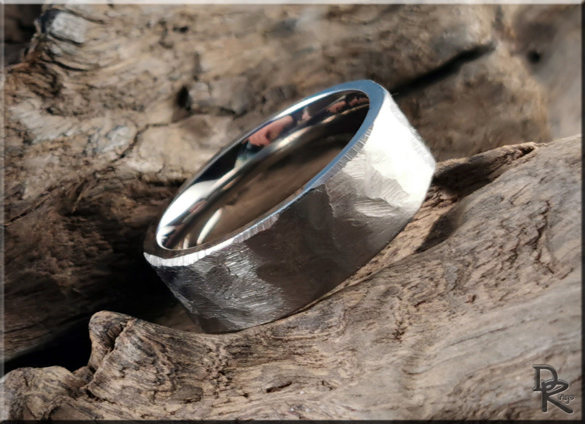Hammered titanium ring with textured finish resting on natural wood surface by DR Rings