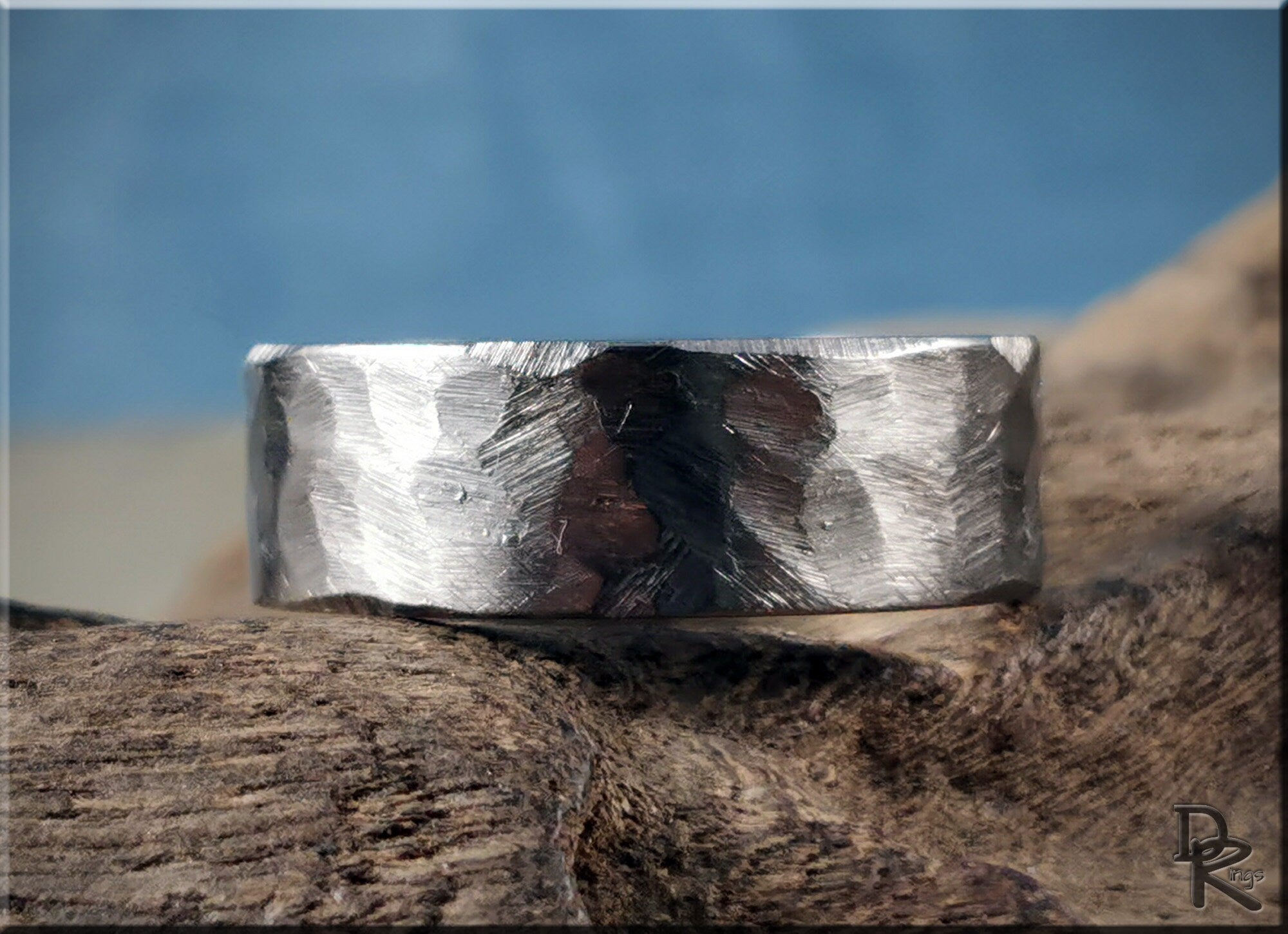 Hammered titanium ring by DR Rings with textured silver finish resting on natural wood surface
