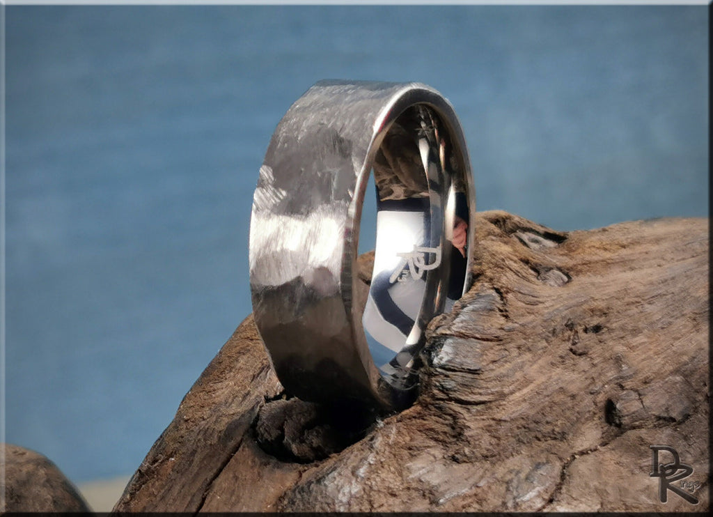 Hammered titanium ring by DR Rings with a textured matte finish resting on rustic wood