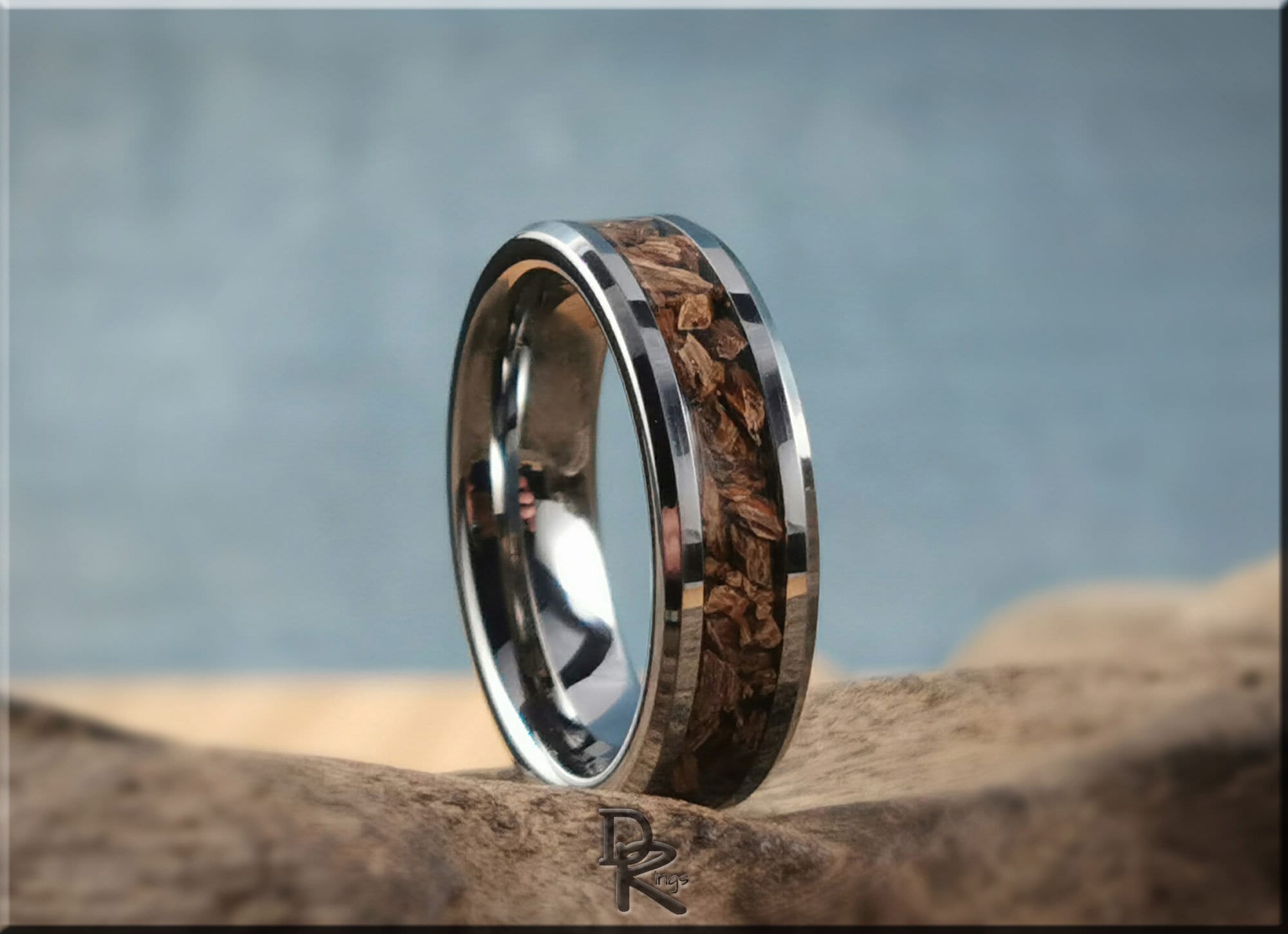 Tungsten ring with dinosaur bone inlay featuring polished silver edges on natural wood background