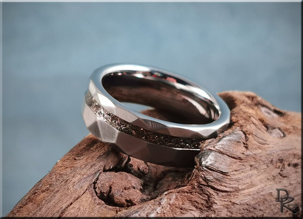 Hammered tungsten carbide ring with meteorite inlay resting on textured wood surface by DR Rings