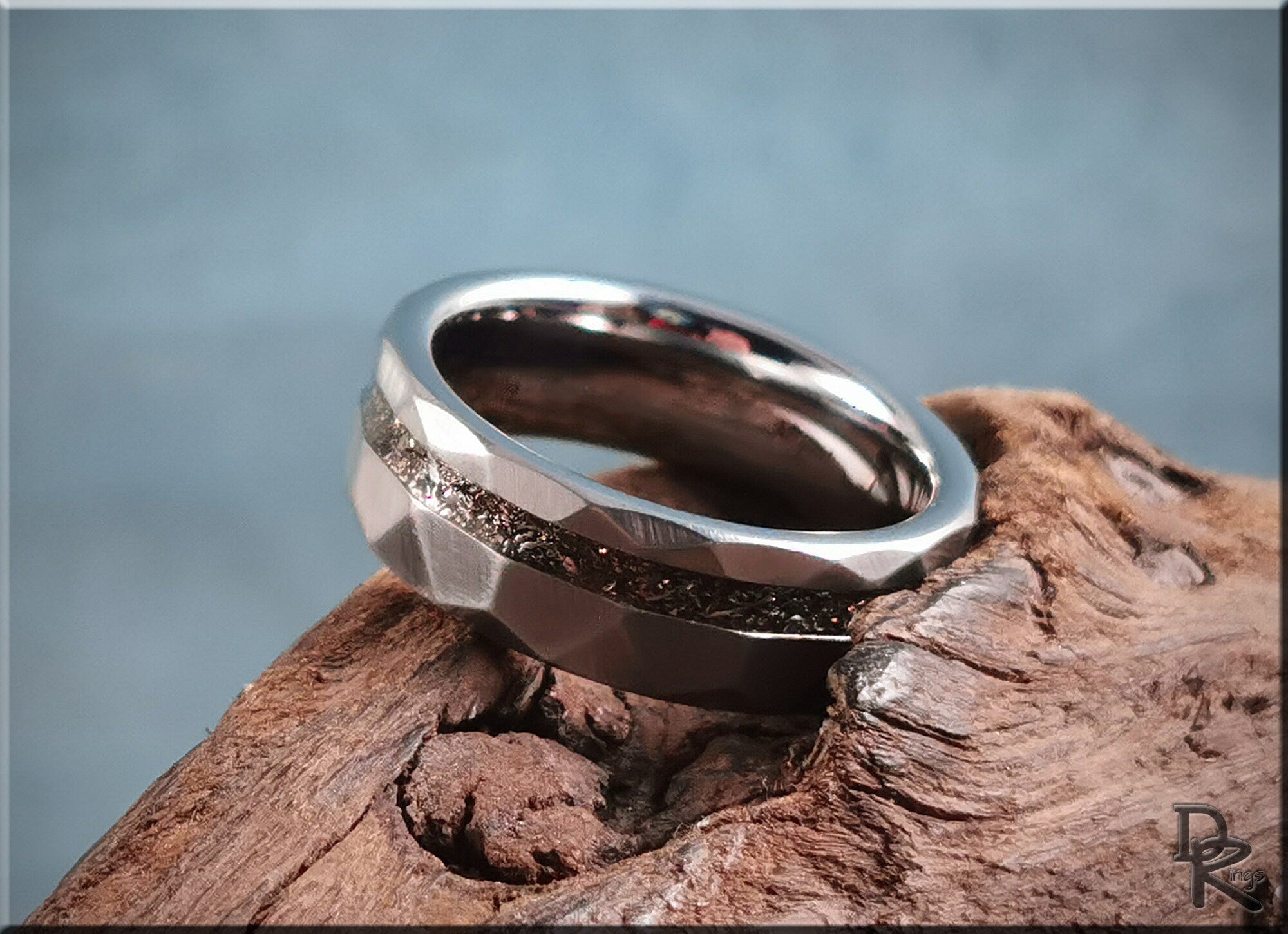 Hammered tungsten carbide ring with meteorite inlay resting on textured wood surface by DR Rings