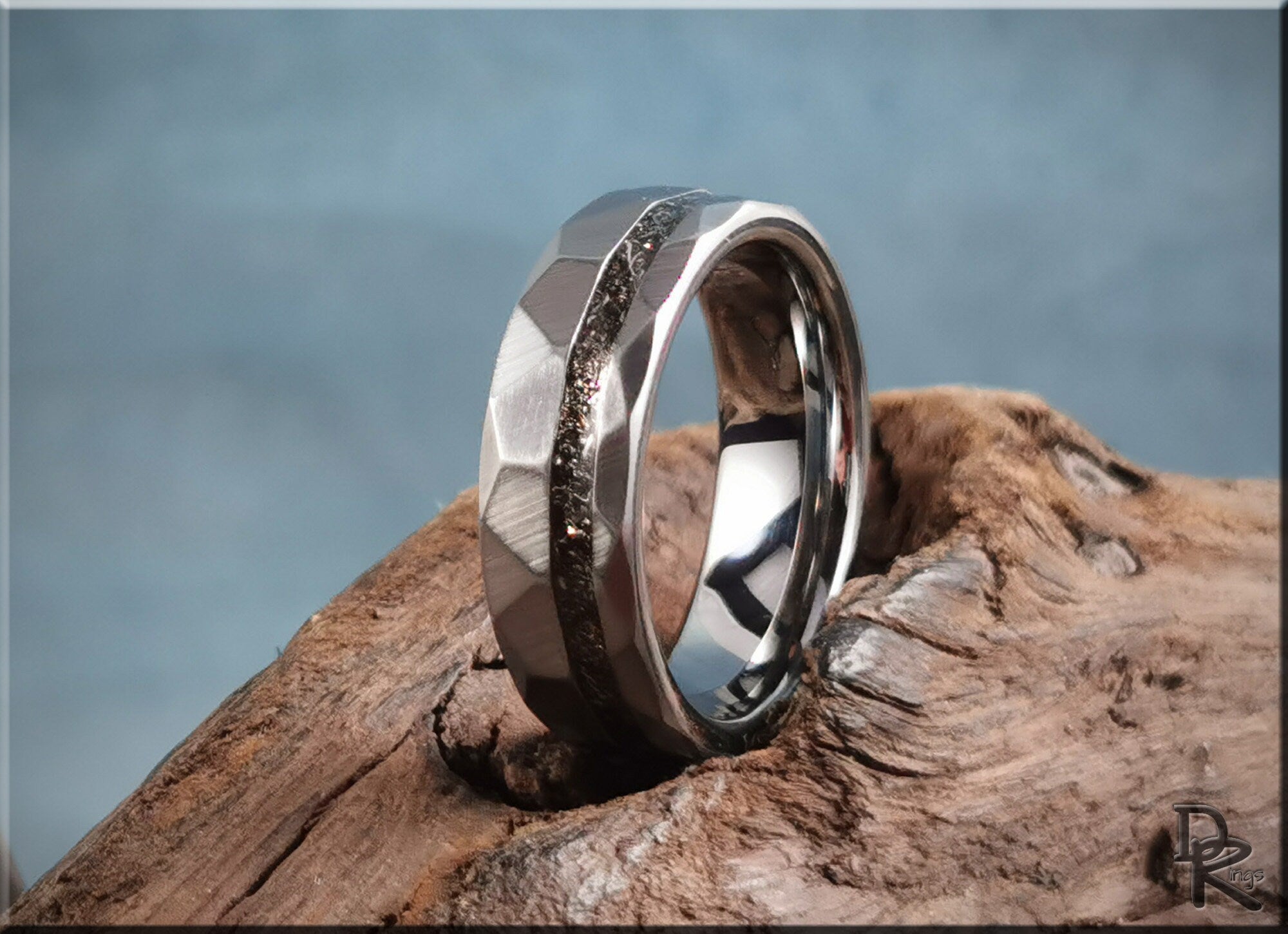 Hammered tungsten carbide ring with meteorite inlay displayed on textured wood by DR Rings