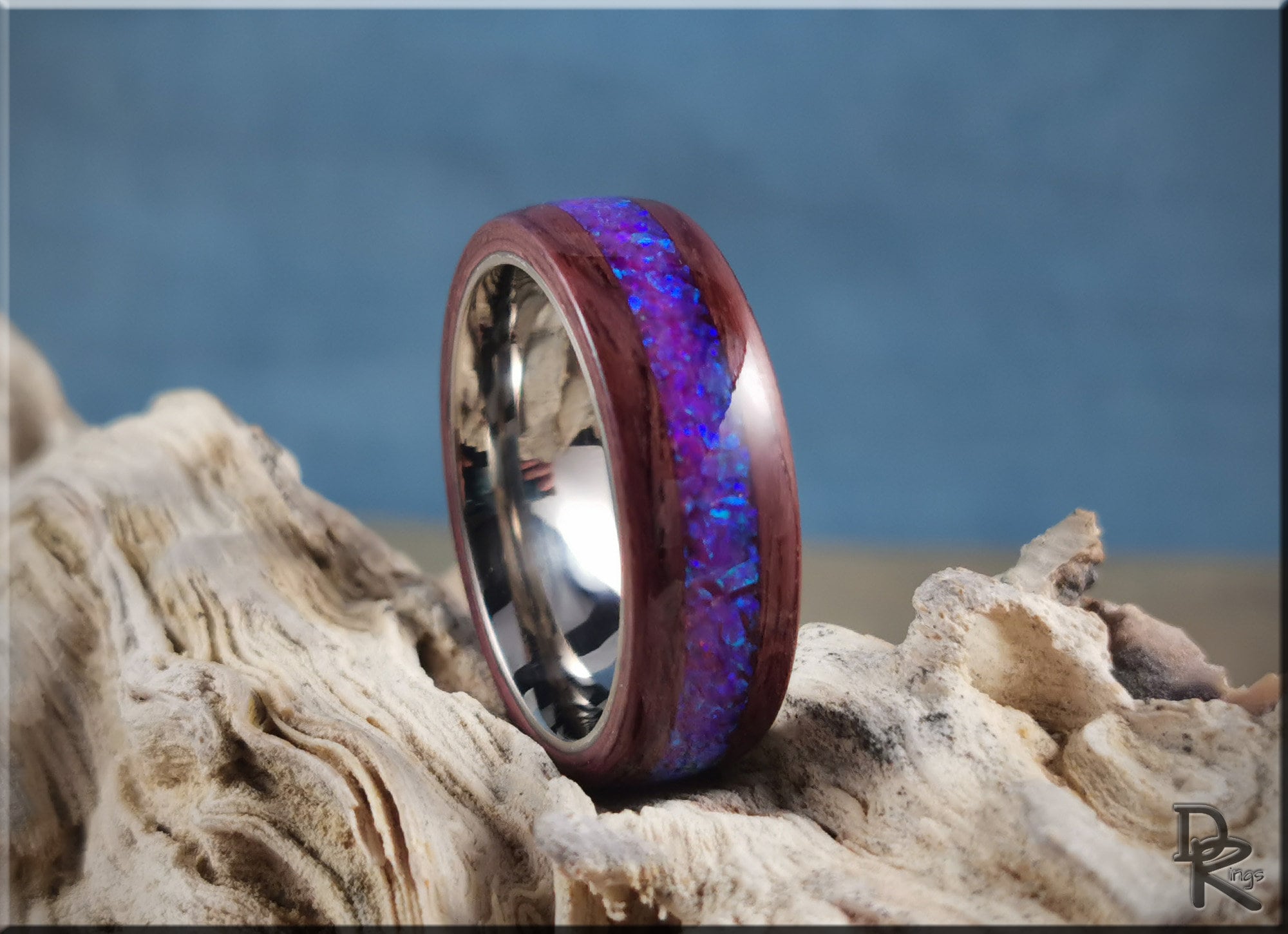 Purpleheart wood ring with opal inlay featuring vibrant blue and purple tones on natural driftwood