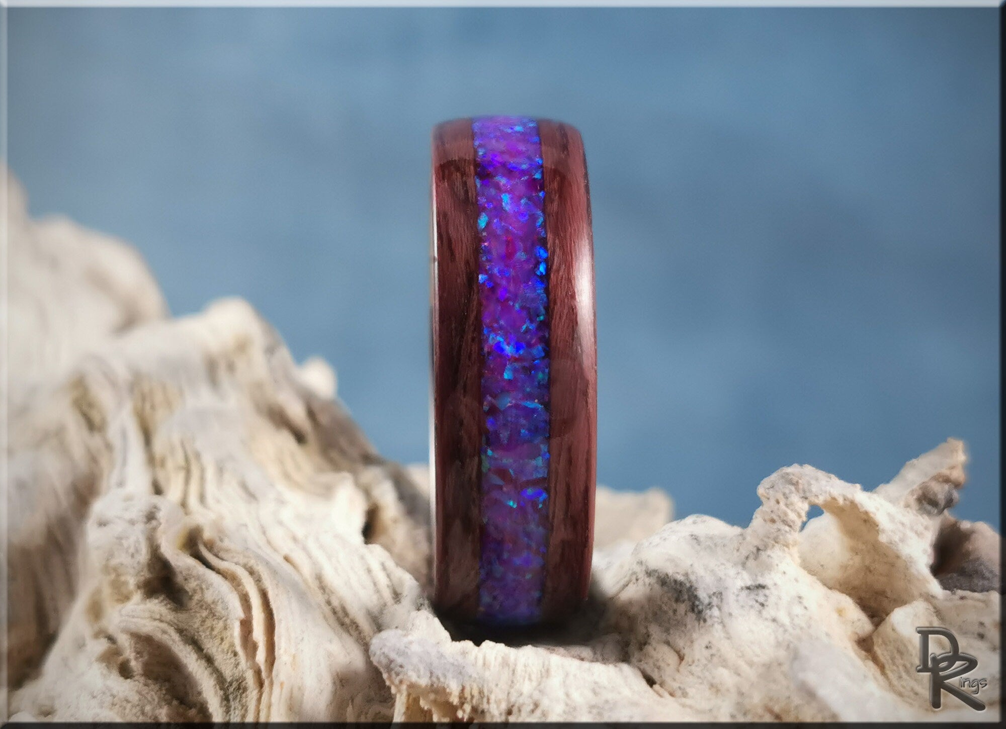 Purpleheart wood ring with opal inlay featuring vibrant blue and purple colors on natural textured background