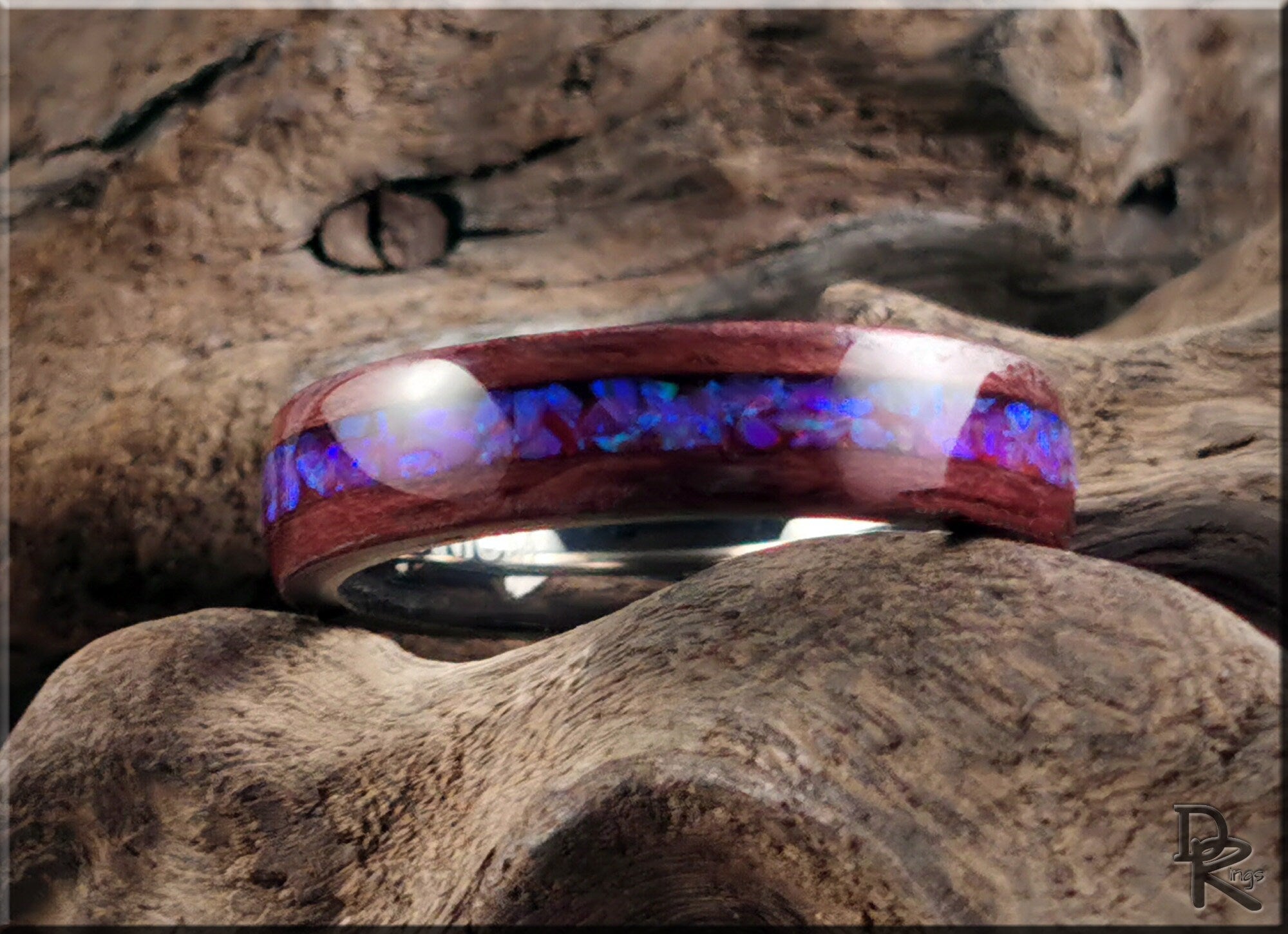 Purpleheart wood ring with opal inlay resting on textured natural wood by DR Rings