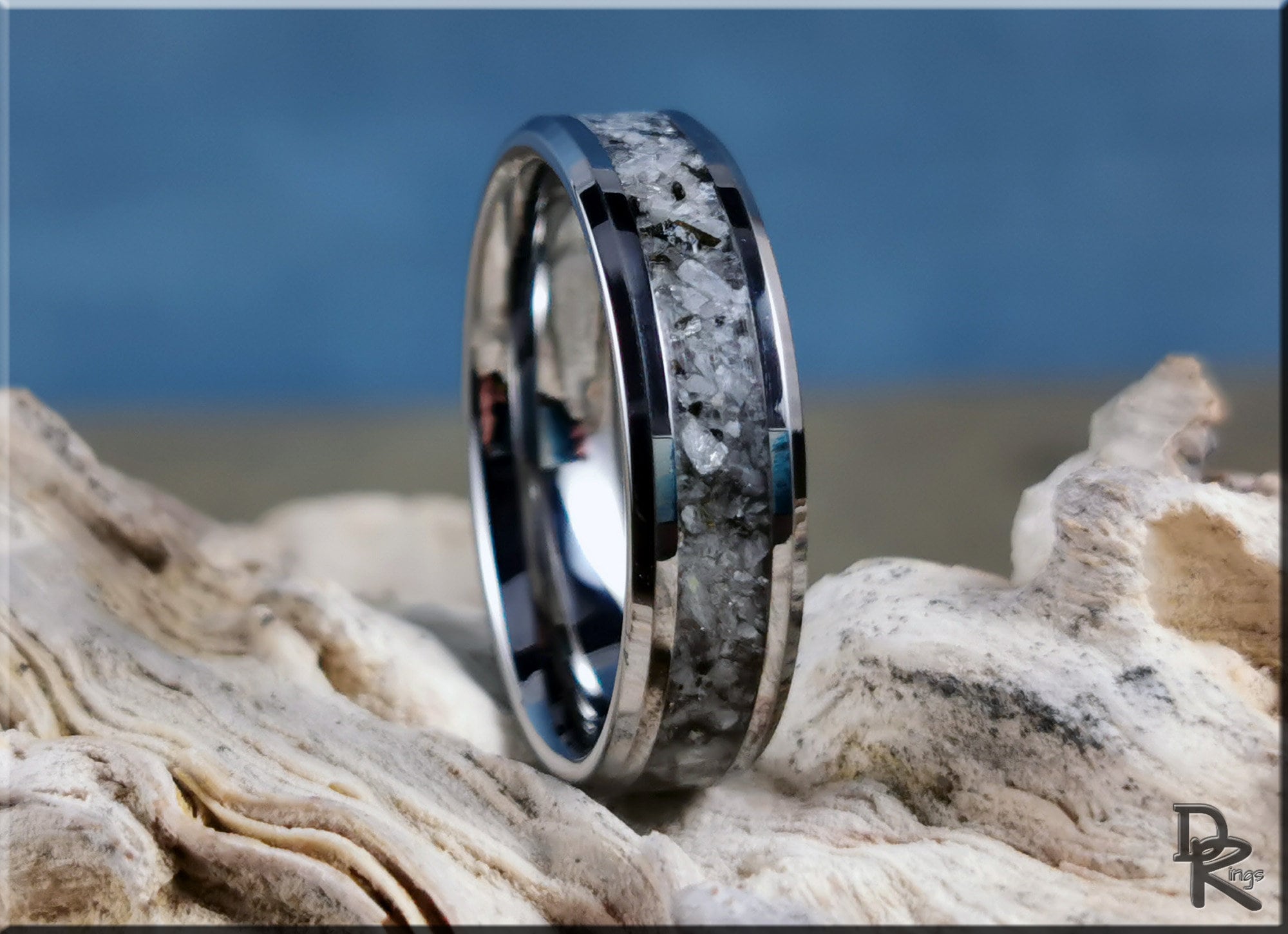 Tungsten ring with moonstone inlay resting on textured natural stone background by DR Rings