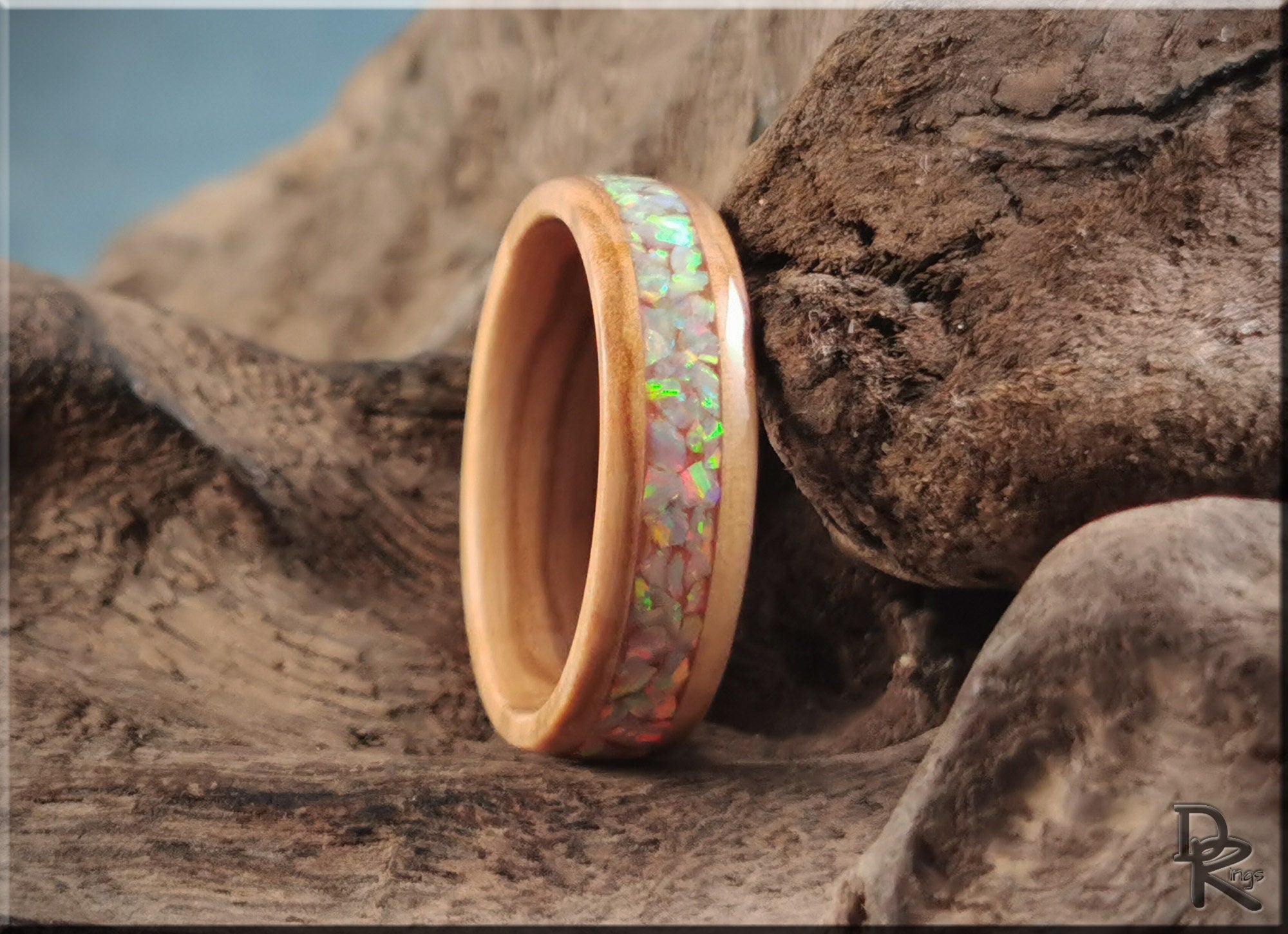 Wooden ring with a colorful iridescent ring opal inlay by DR Rings on rustic wood background
