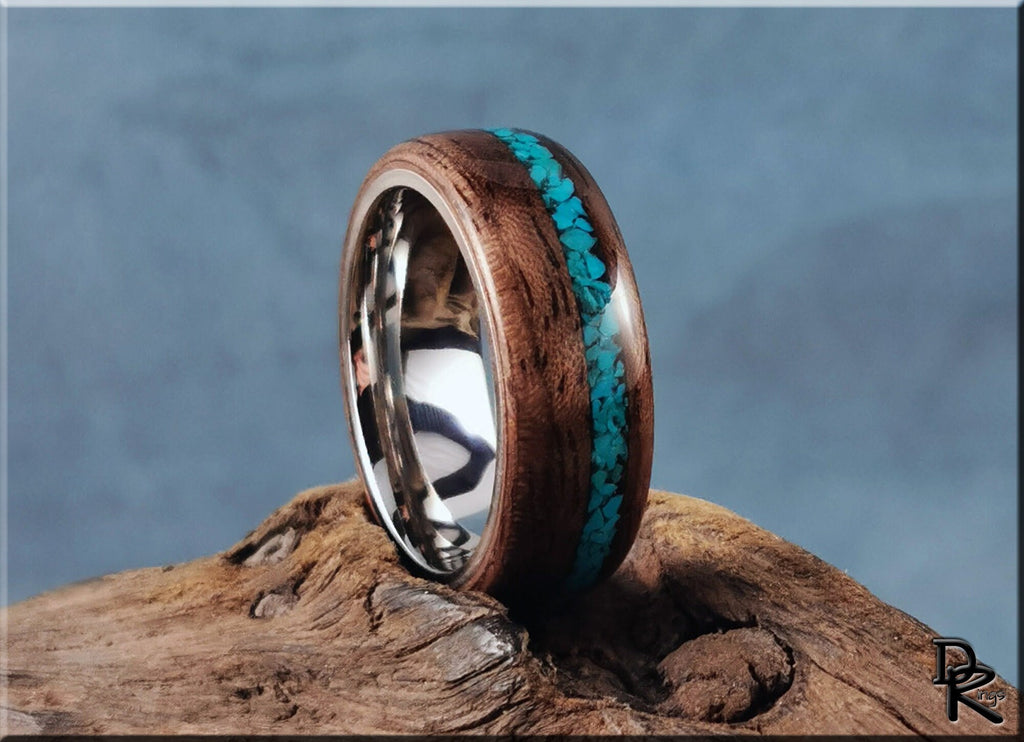 Walnut ring with turquoise inlay by DR Rings on a rustic wooden surface with a blurred blue background