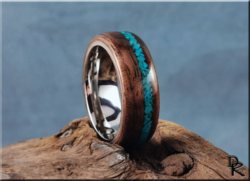Walnut ring with turquoise inlay by DR Rings on a rustic wooden surface with a blurred blue background
