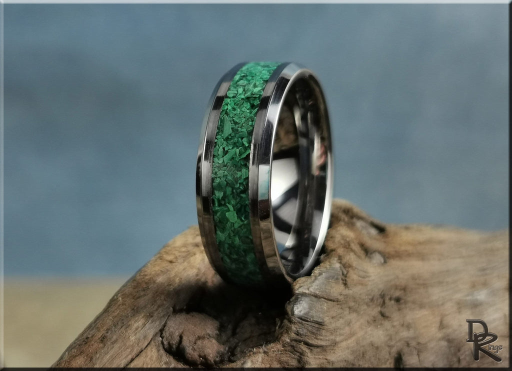 Tungsten ring with green malachite inlay resting on natural wood surface