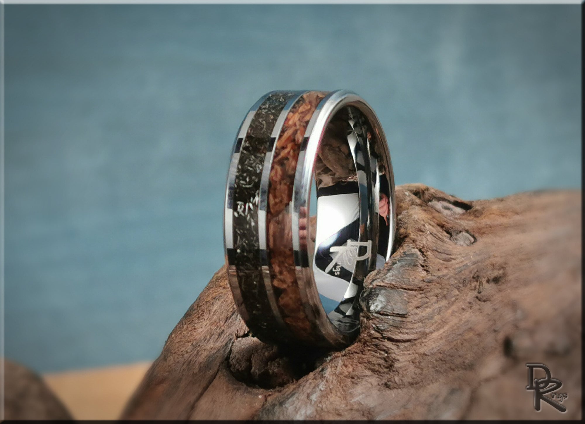 Tungsten ring with inlays featuring wood and dark stone accents by DR Rings on rustic wood background