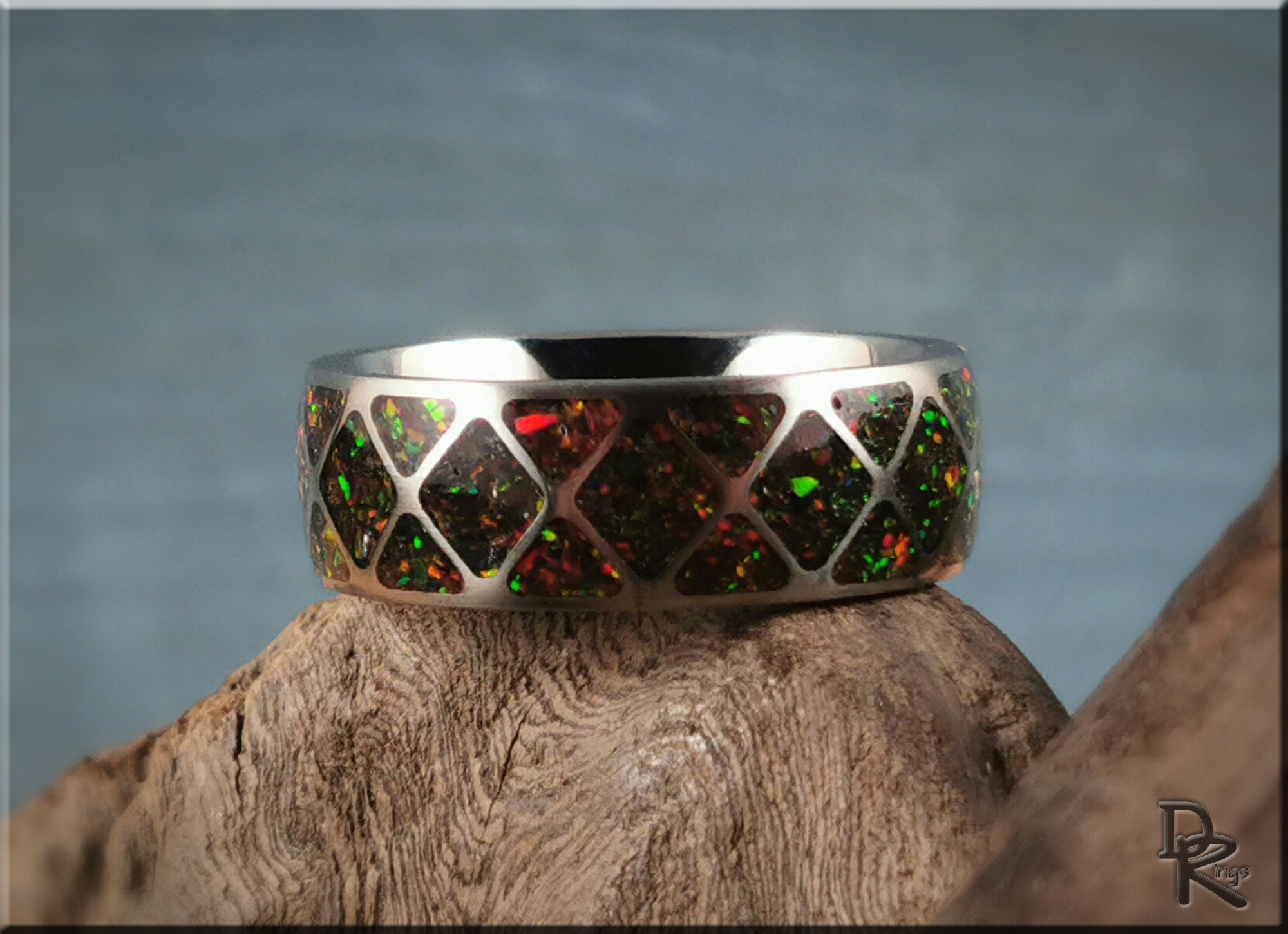 DR Rings titanium ring with opal inlay featuring red and green diamond pattern on wood background