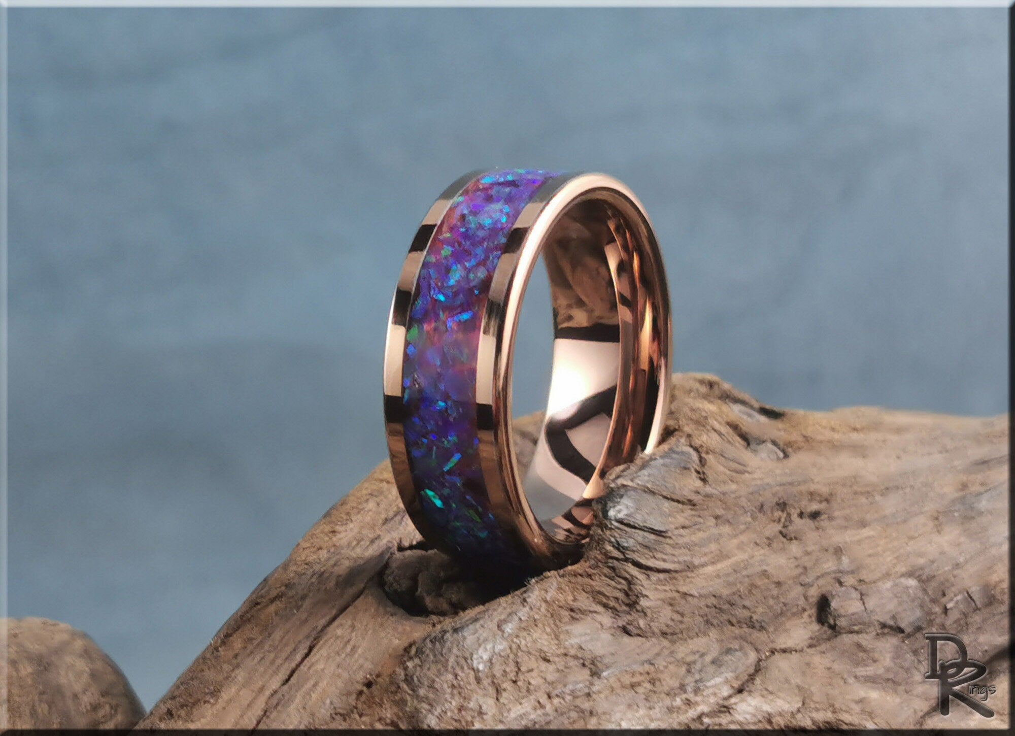 Rose tungsten ring with opal inlay featuring vibrant blue and purple hues on a natural wood surface