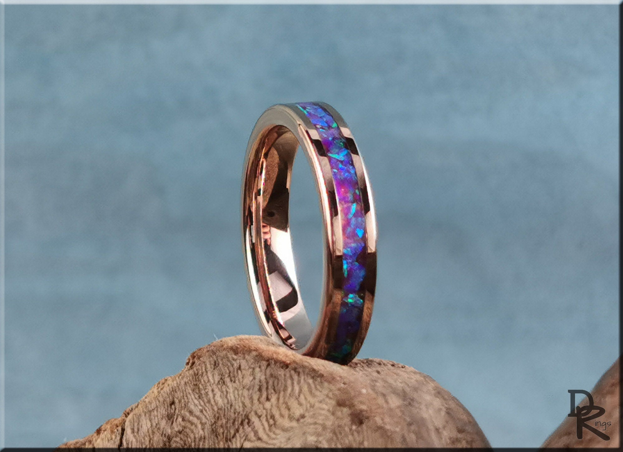 Rose tungsten ring with opal inlay featuring vibrant blue and purple stones on a wooden surface