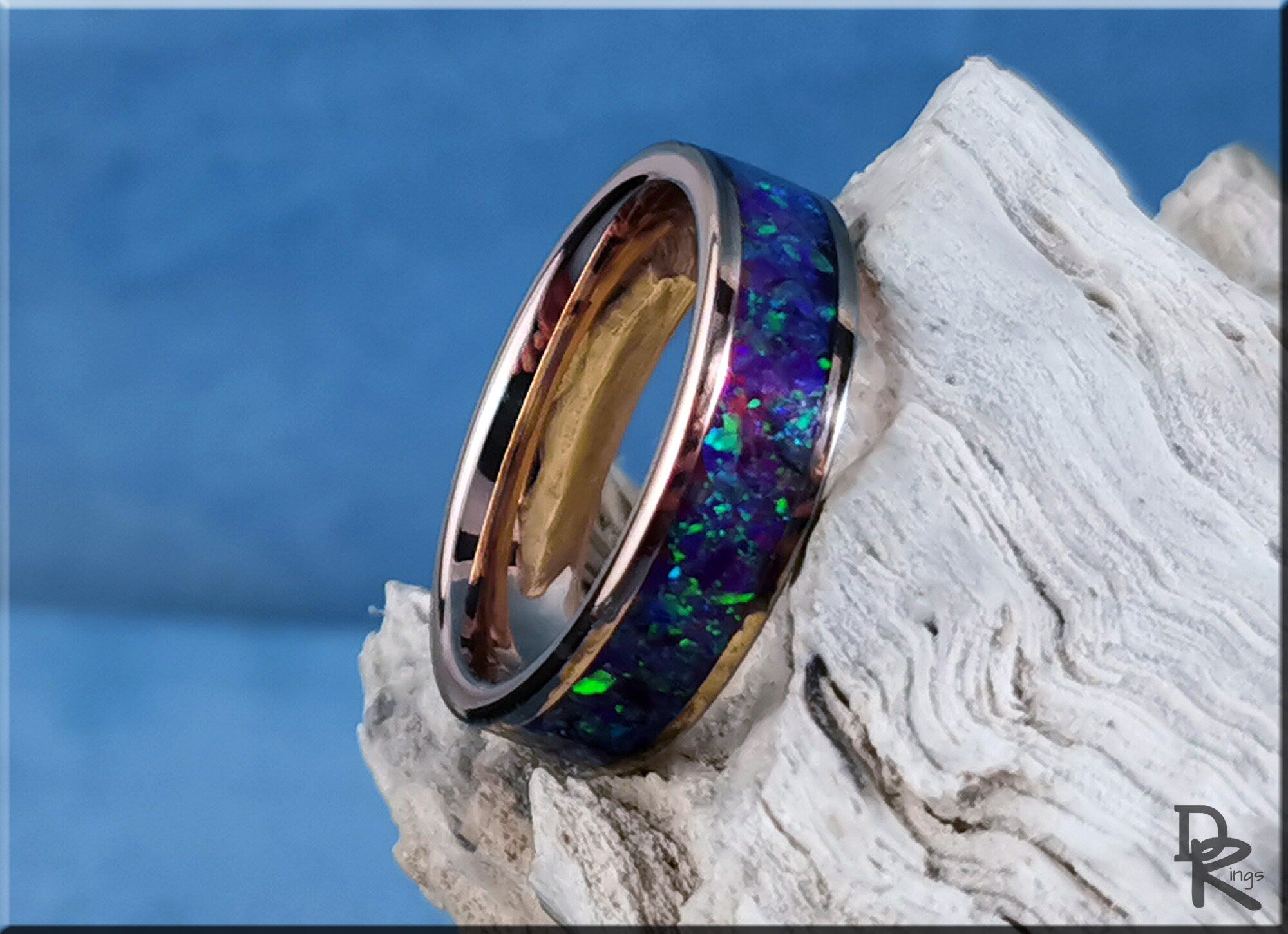 Rose tungsten ring with opal inlay featuring vibrant blue and green stones on textured background