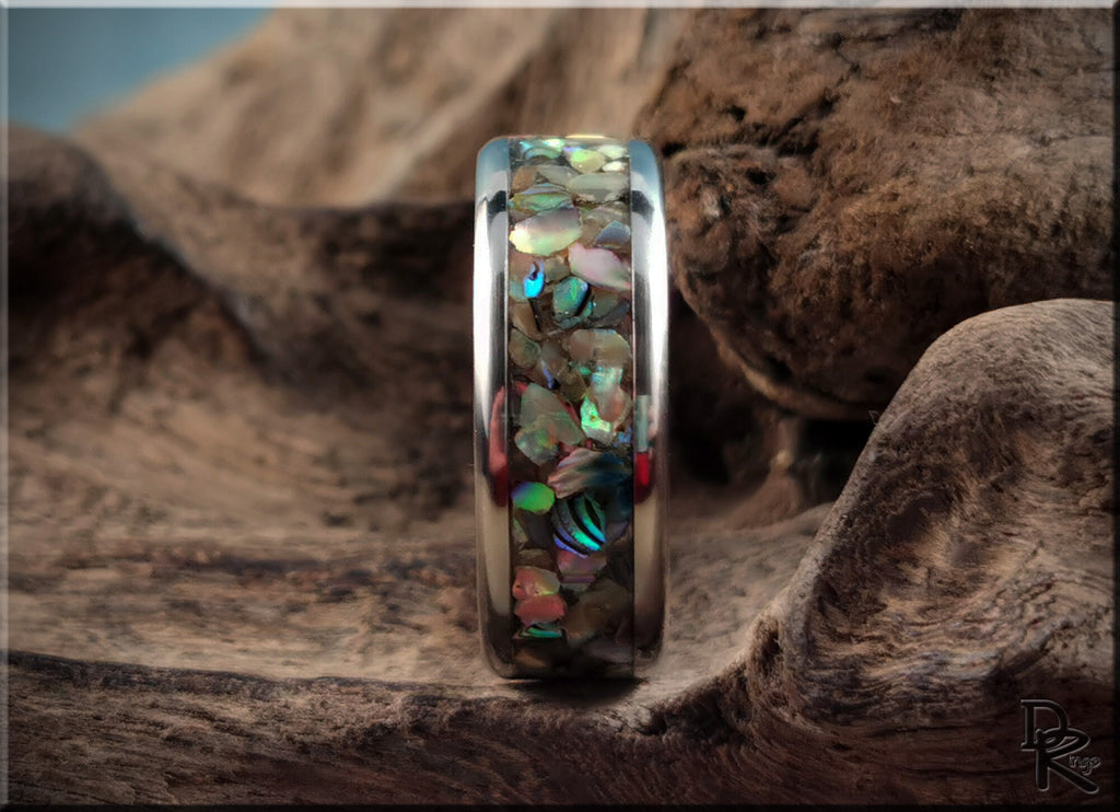 DR Rings titanium ring with abalone inlay featuring iridescent shell pieces on natural wood background