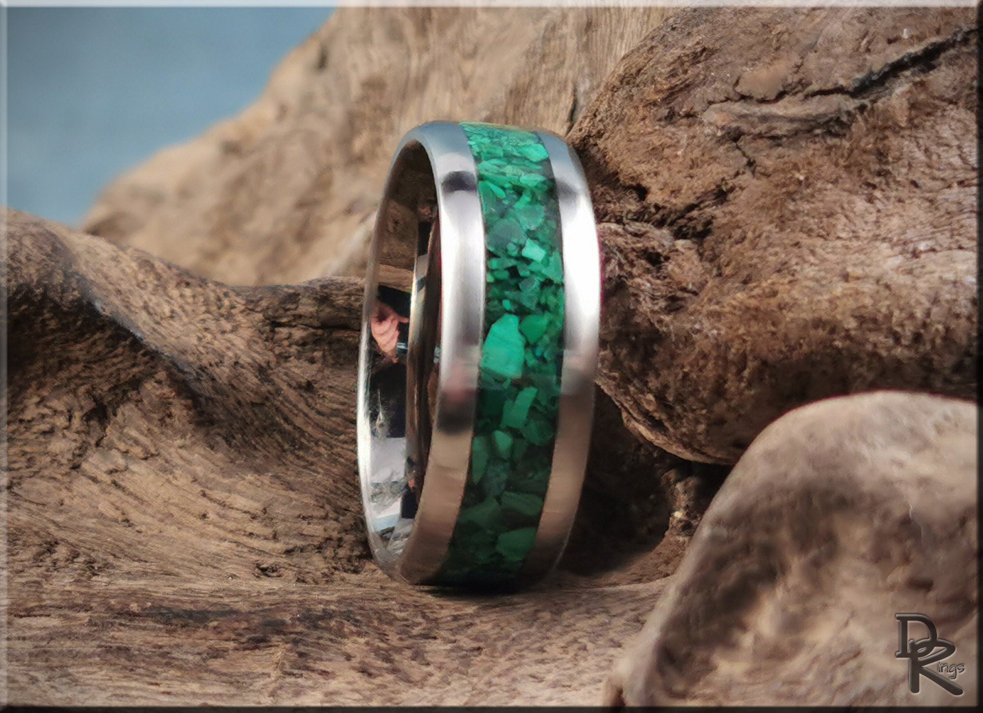 Titanium ring with malachite inlay featuring vibrant green stone in center on rustic wood background