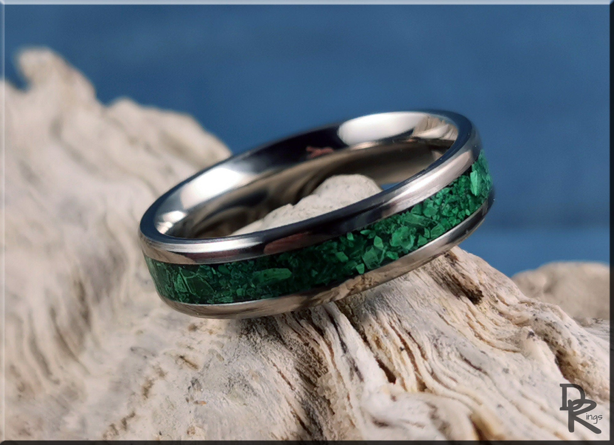 Titanium ring with malachite inlay resting on textured driftwood against a blue background