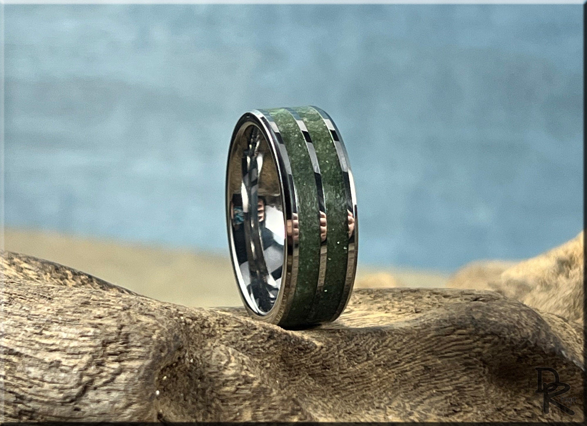 DR Rings tungsten ring carbide with emerald green inlay resting on textured wood surface