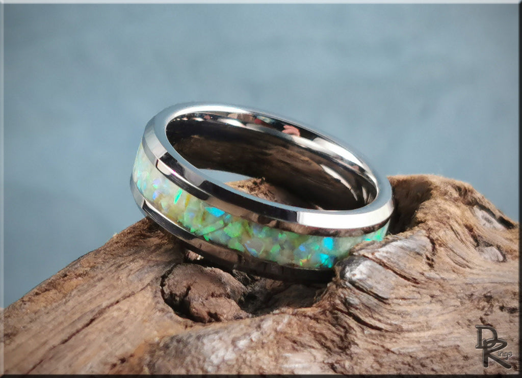 Tungsten ring with opal and glow inlay featuring bright green and blue hues on wood background