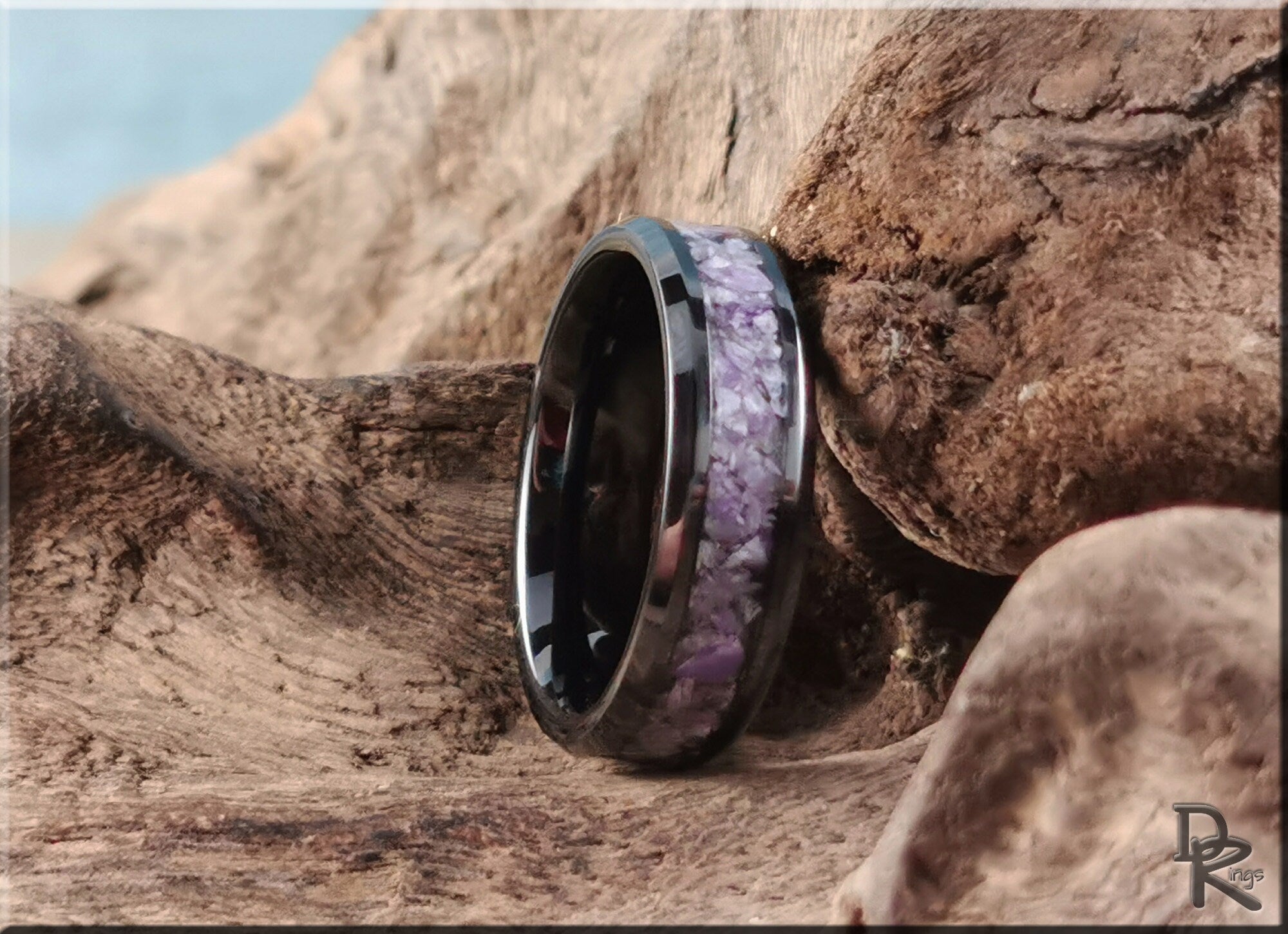 Ceramic ring with charoite inlay featuring purple stones resting on textured natural wood