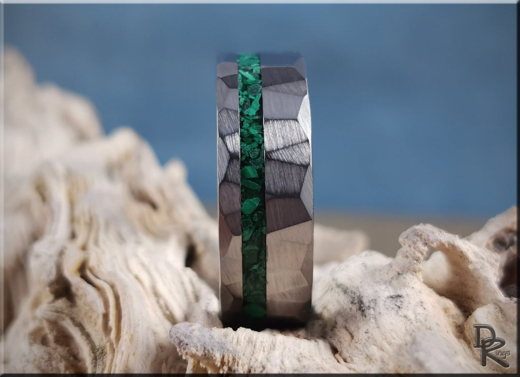 Hammered tungsten ring with malachite green inlay displayed on textured natural stones