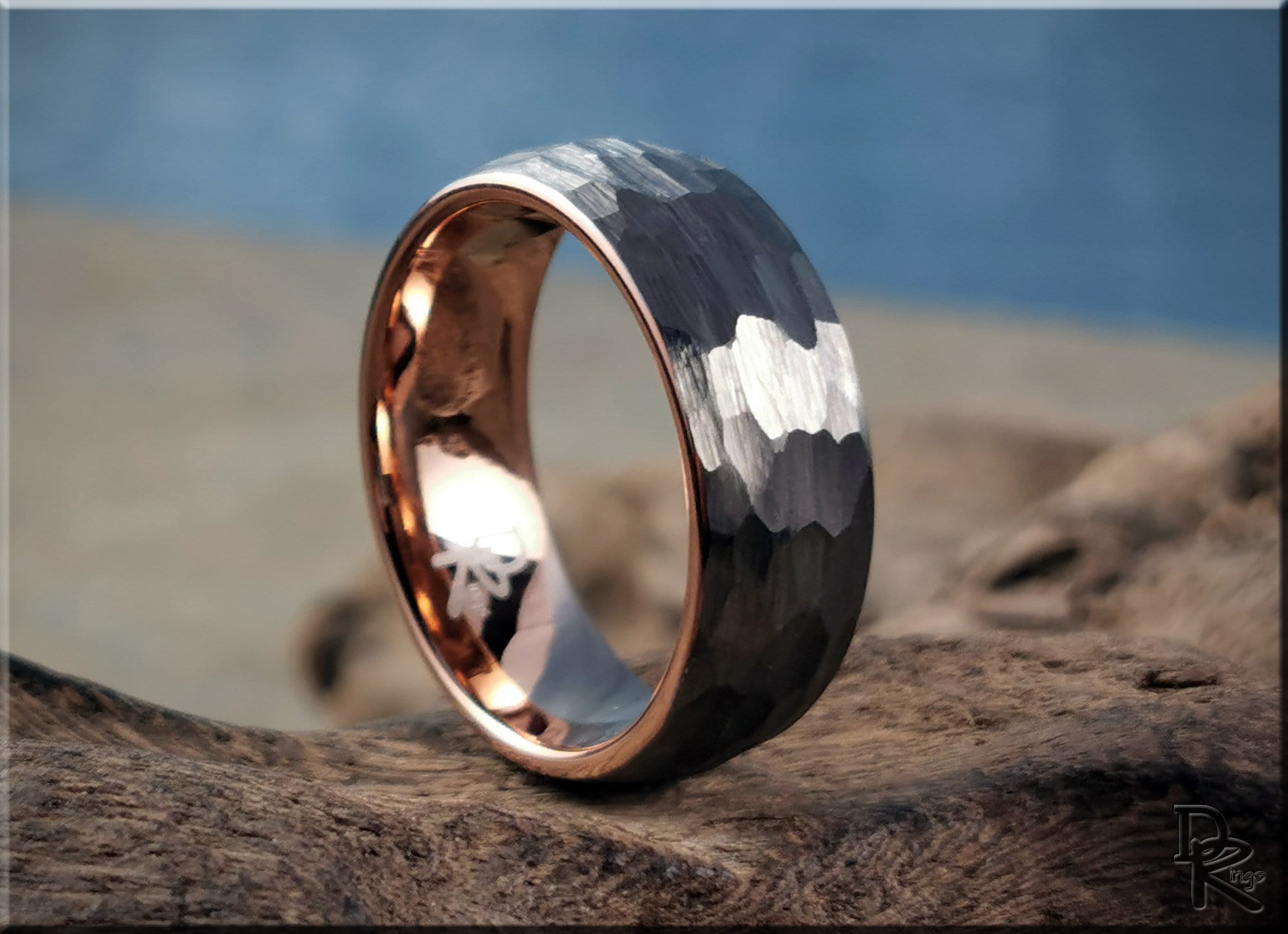Hammered tungsten ring with rose gold core displayed on natural wood background by DR Rings