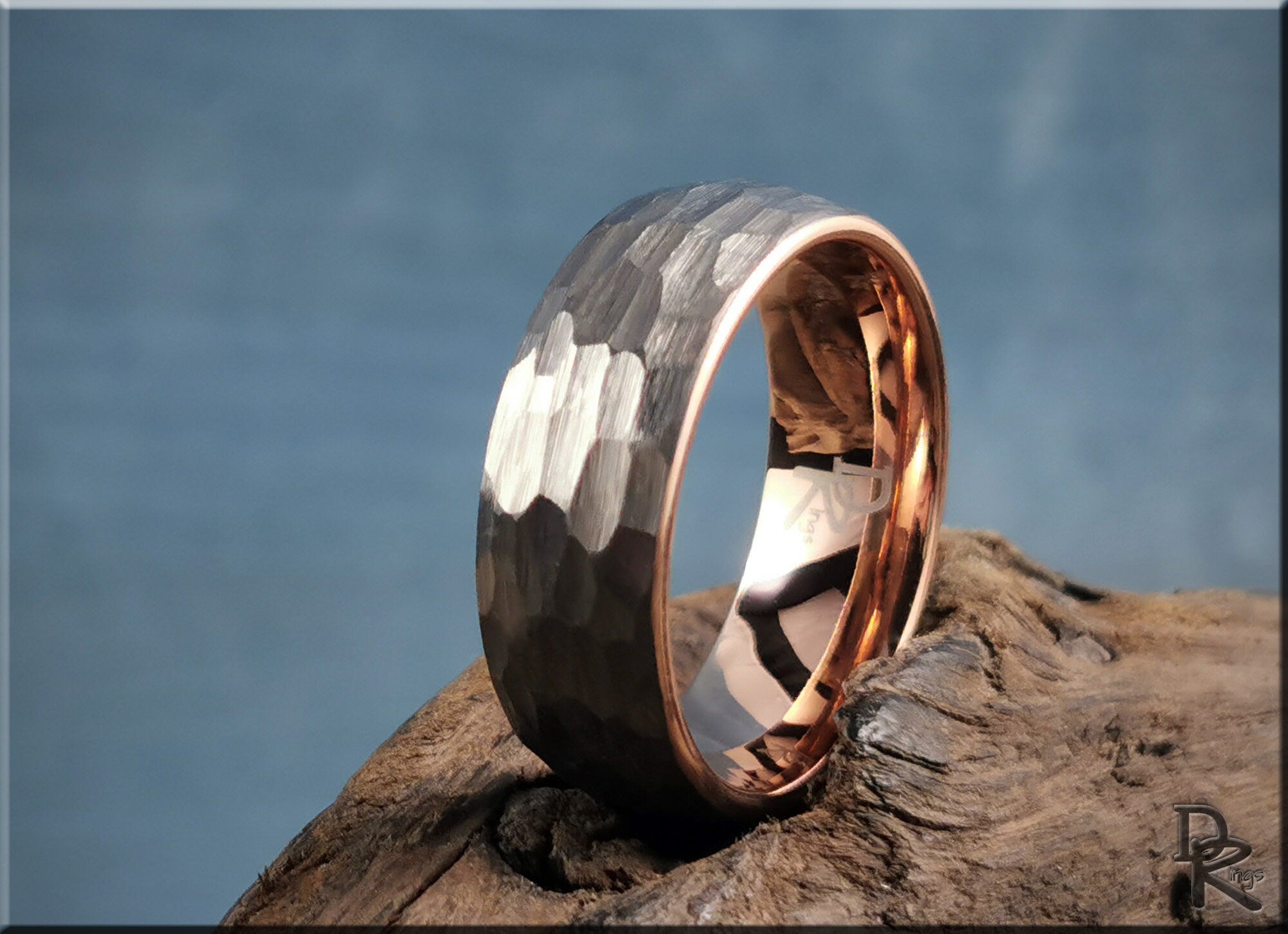 Hammered tungsten ring with rose gold core displayed on rustic wood background by DR Rings