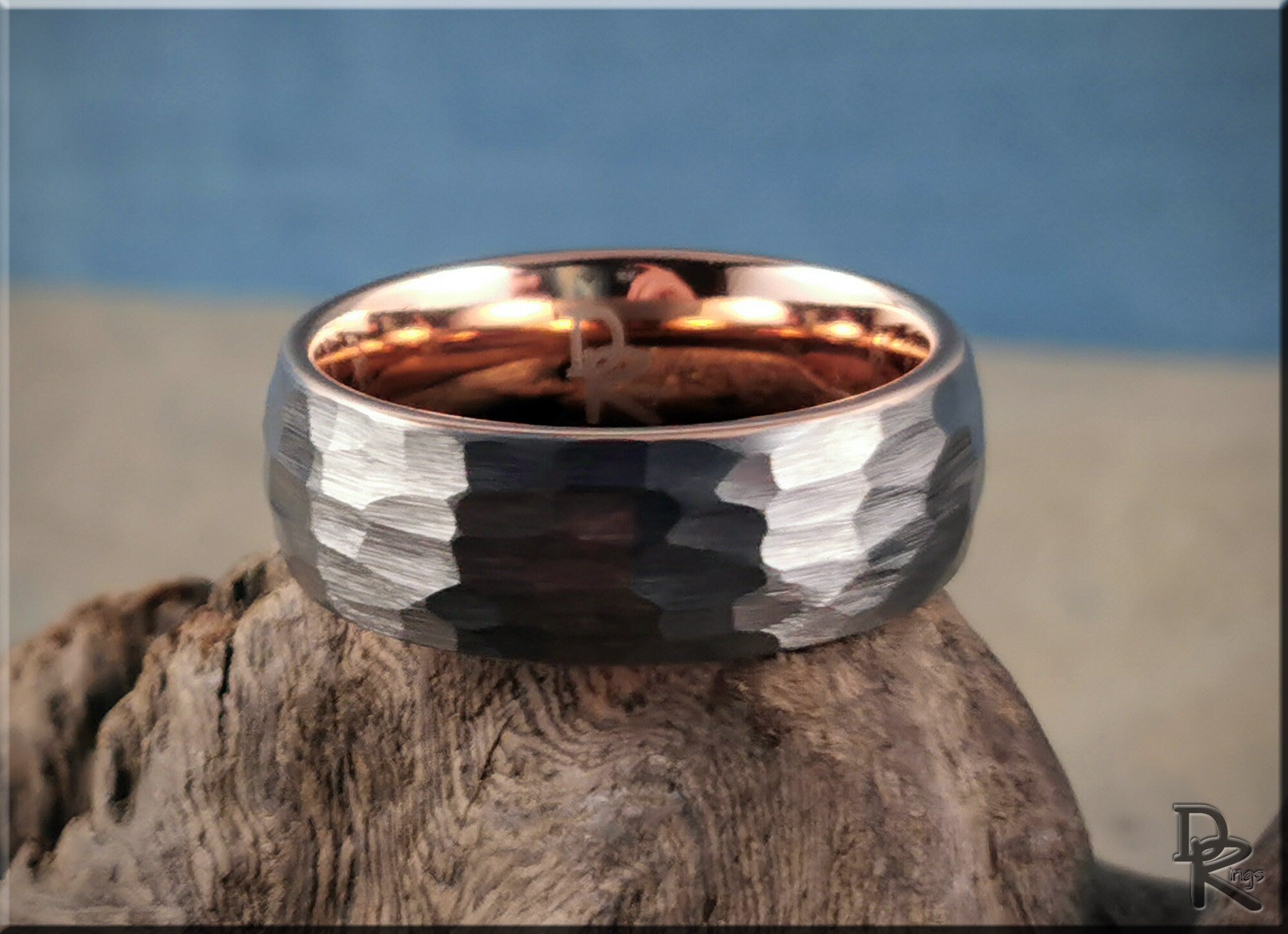 Hammered tungsten ring with rose gold core resting on textured wood background from DR Rings
