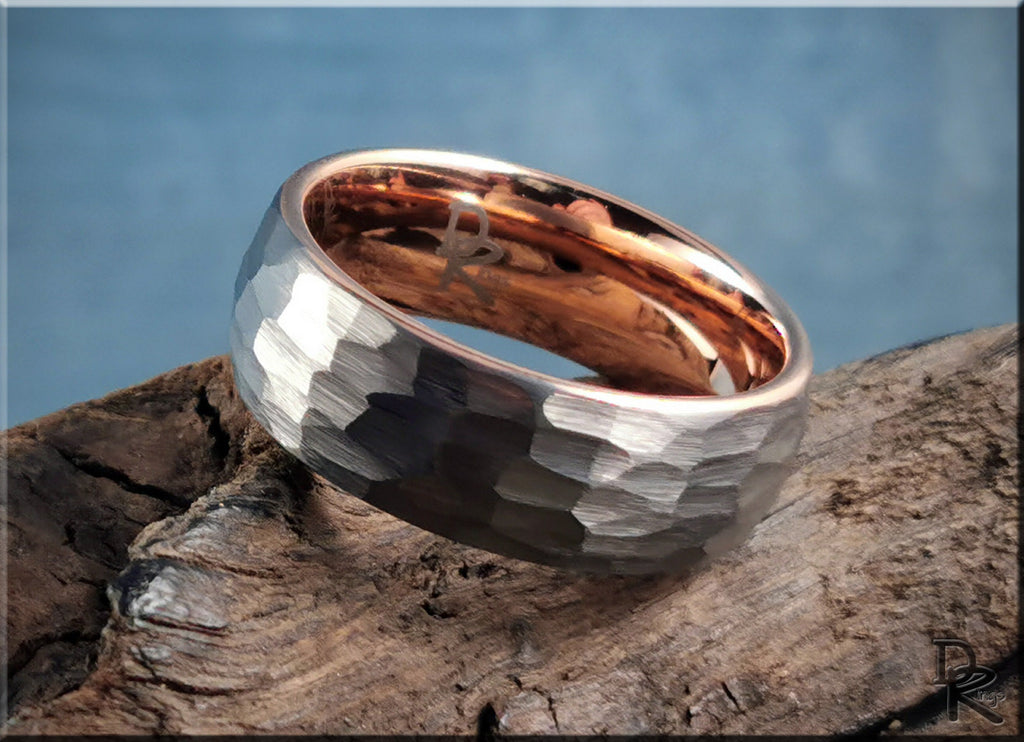Hammered tungsten ring with rose gold core by DR Rings displayed on textured wood background