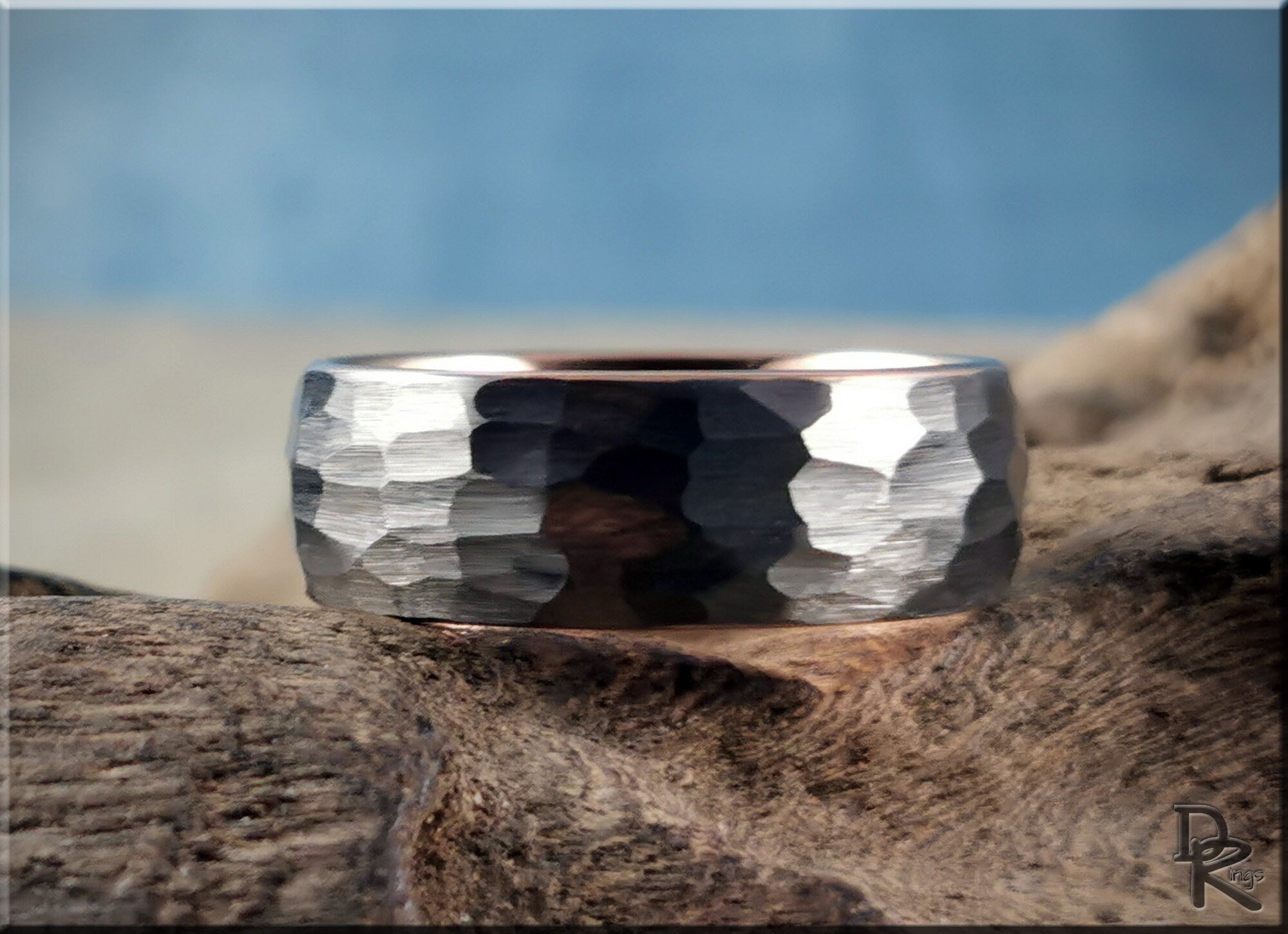 Hammered tungsten ring with rose gold core featuring a textured silver exterior on wood