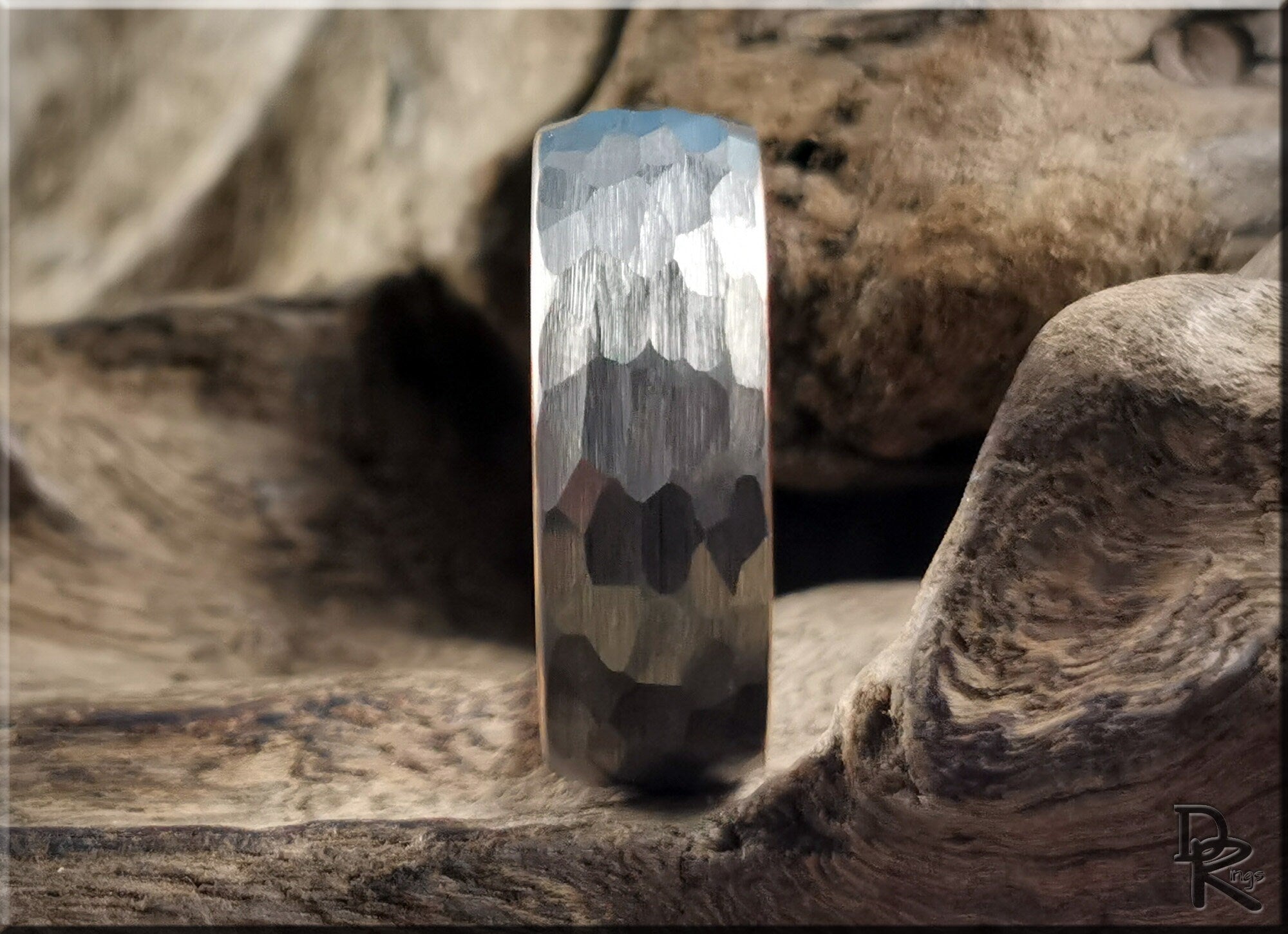 Hammered tungsten ring with rose gold core displayed on textured wood background by DR Rings