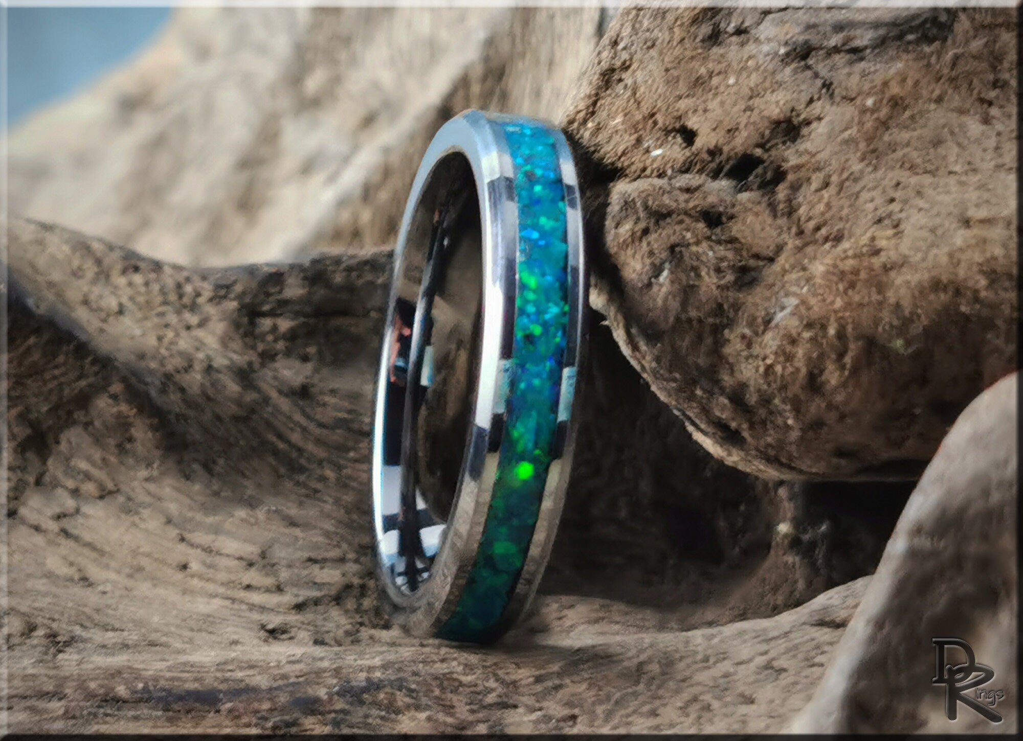 Tungsten carbide ring with opal inlay featuring vibrant blue and green colors on rustic wood background