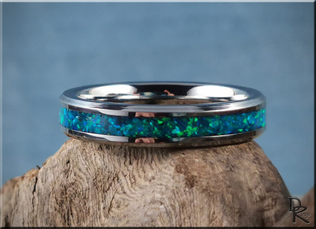 Tungsten carbide ring with opal inlay by DR Rings featuring vibrant blue and green colors on a textured wood surface