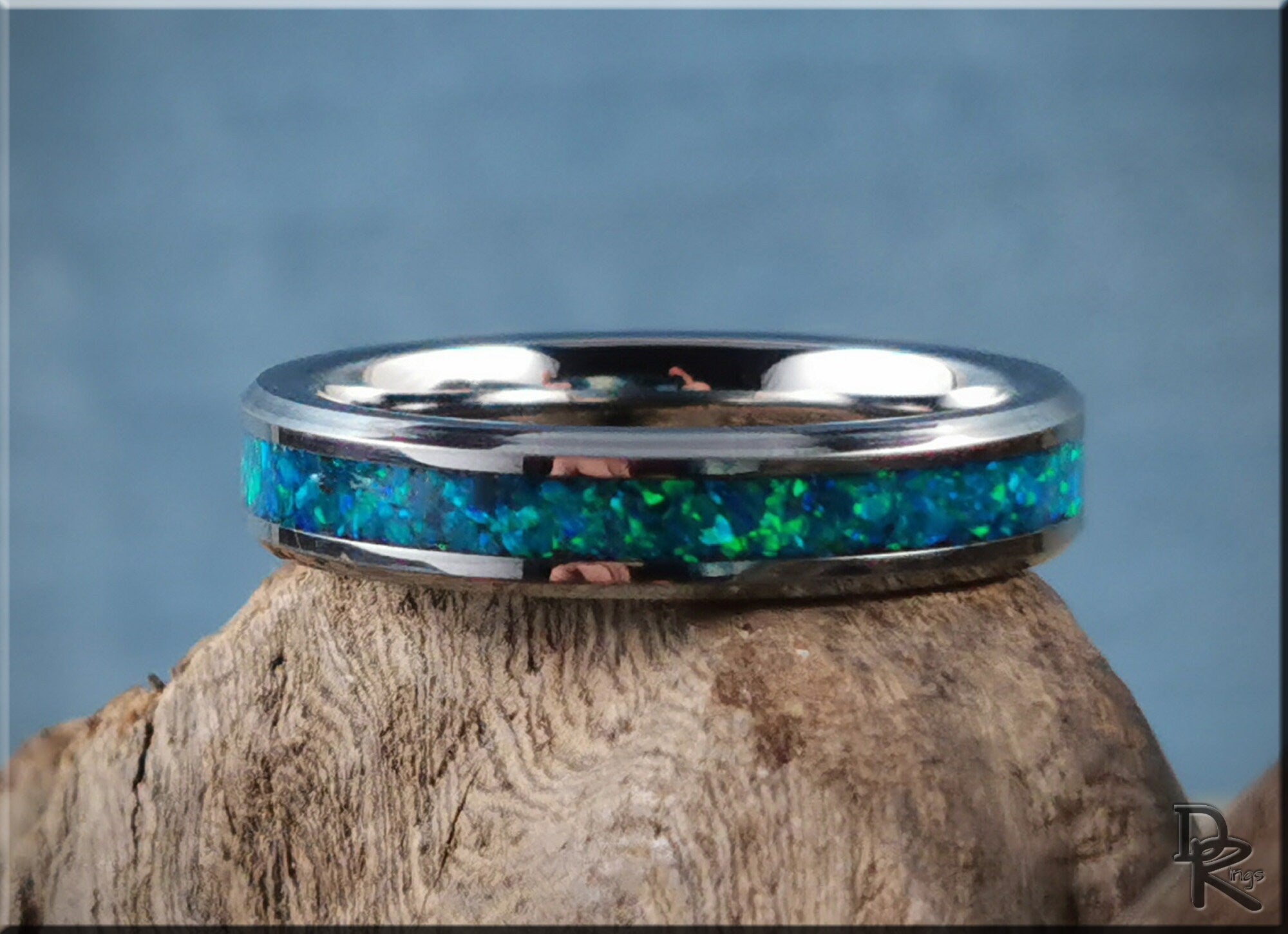 Tungsten carbide ring with opal inlay by DR Rings featuring vibrant blue and green colors on a textured wood surface