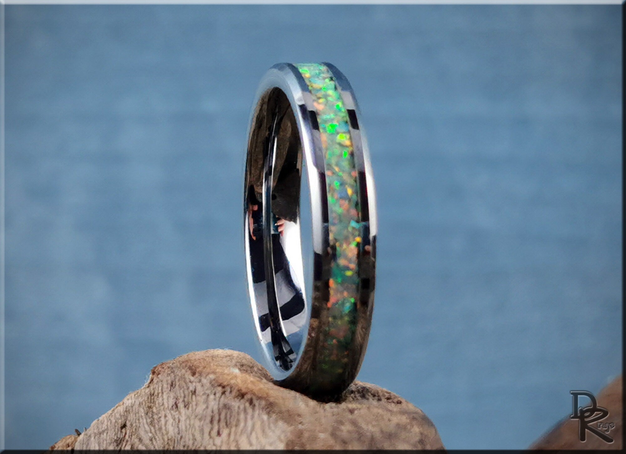 Tungsten carbide ring with opal inlay displaying vibrant green and orange colors on natural wood background