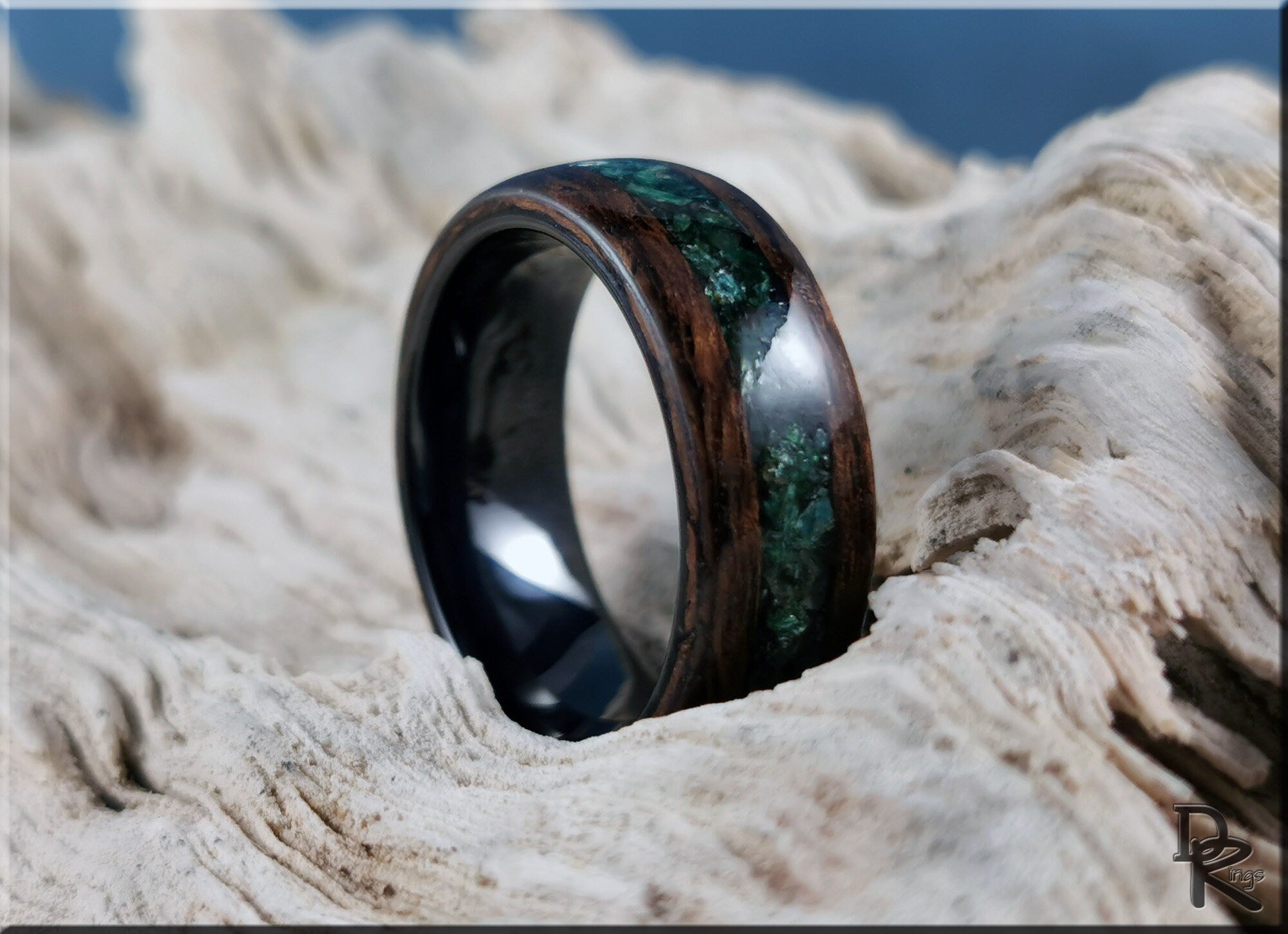 Wood ring with inlay featuring dark wood and green stone detail on natural wooden background