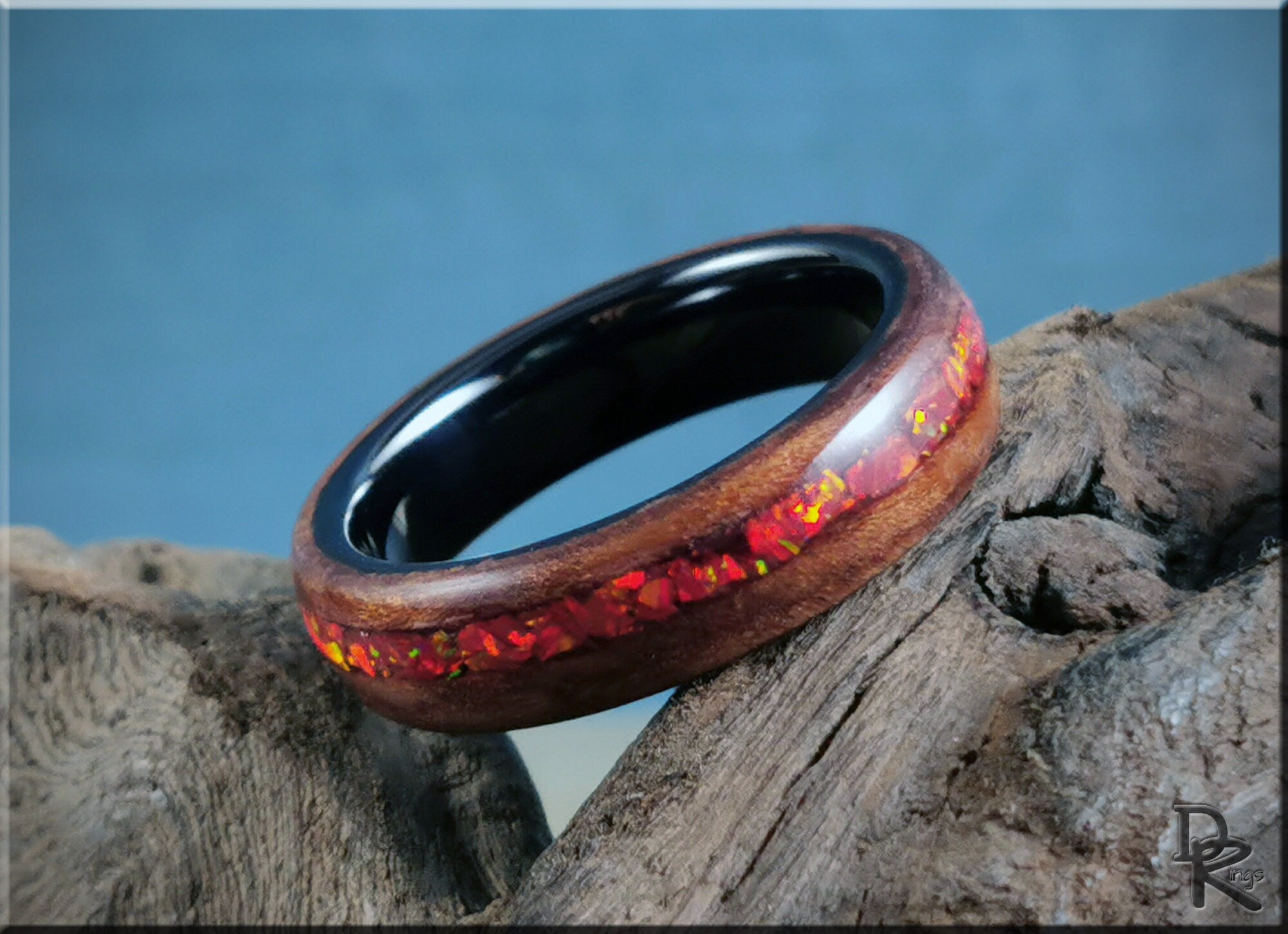 DR Rings wood ring with opal inlay featuring red opal accents and dark inner band on rustic wood
