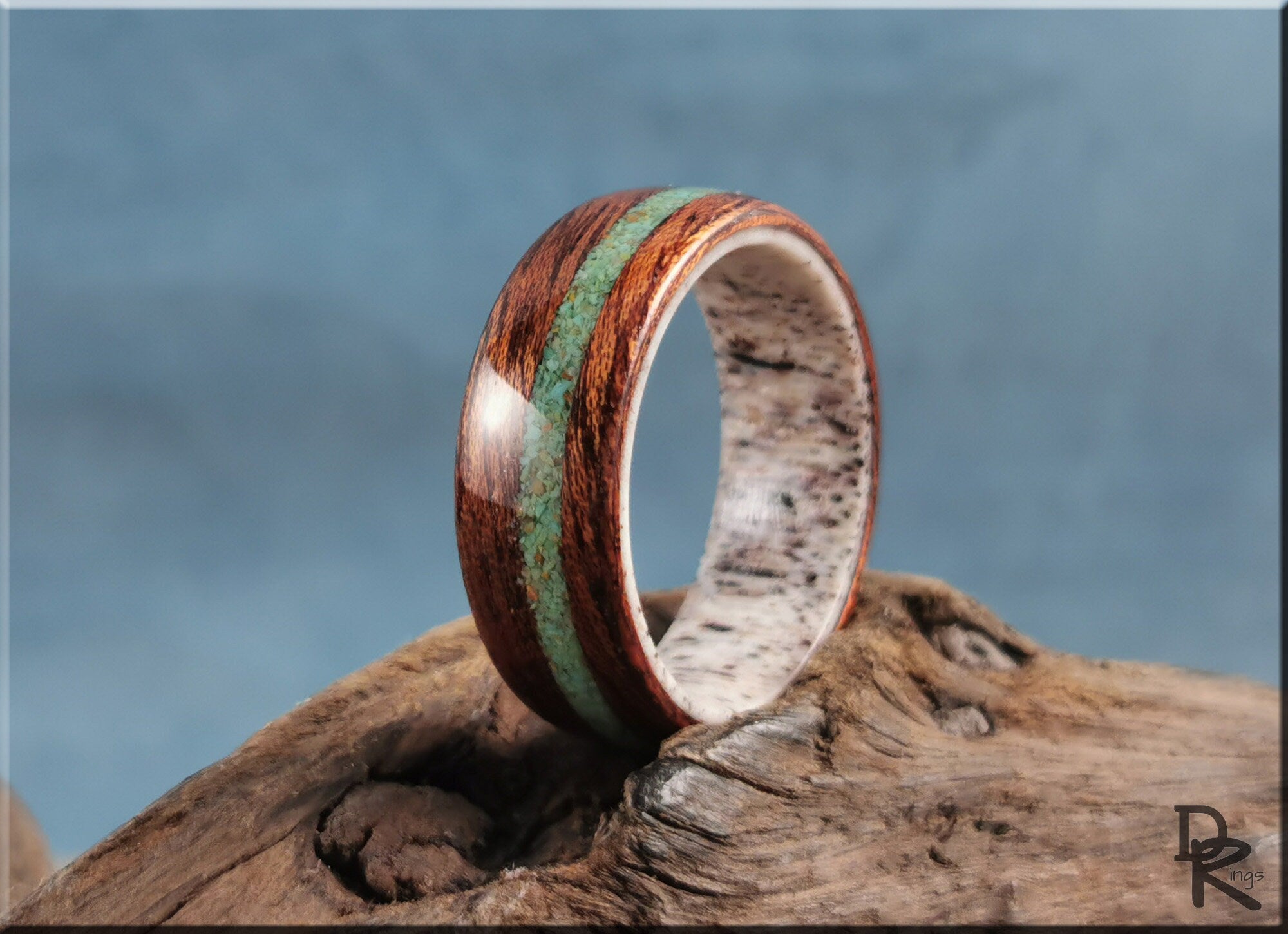 DR Rings wood ring with turquoise and antler inlay resting on a textured wooden surface